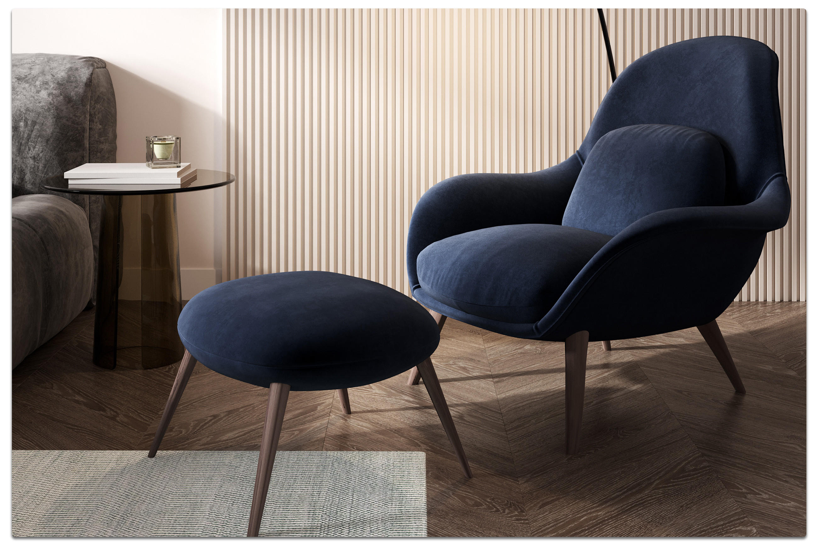 Modernes Interieur mit dunkelblauem Polstersessel und passendem Hocker, rundem Beistelltisch mit Büchern und Kerze – elegantes Wohnambiente mit Holzfußboden im Fischgrätmuster.