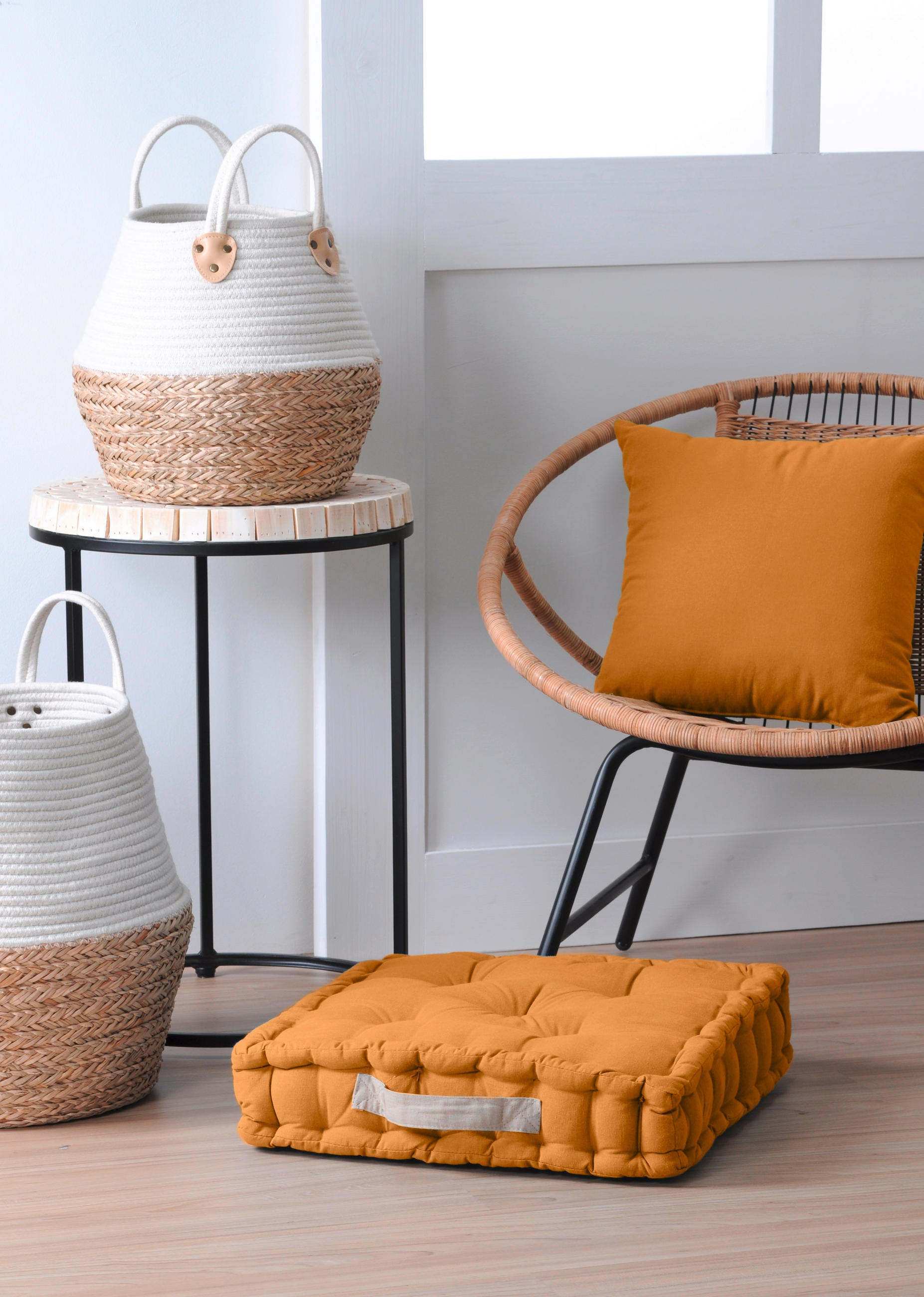  Oranžna blazina na stolu, sedežna blazina na tleh in košara iz vrbovine ob stolu.