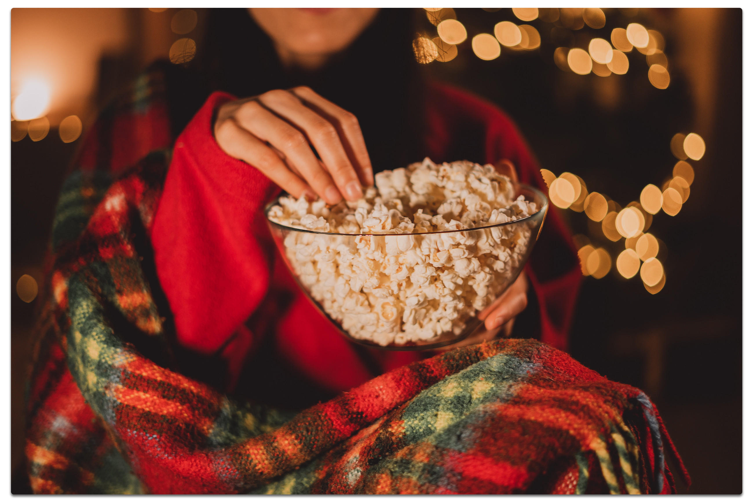 Frau genießt Popcorn vor festlichen Weihnachtslichtern beim Film schauen