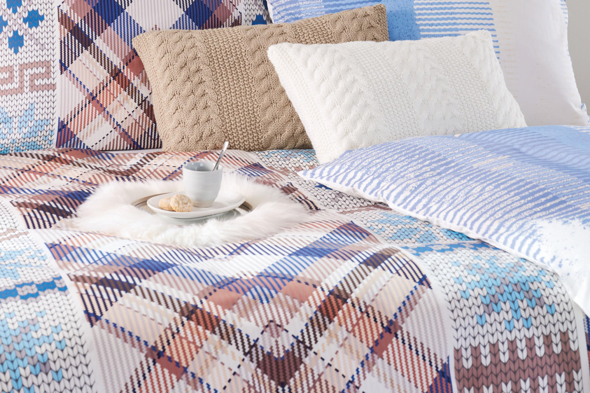 Bett in weiß, blau-weiße Bettwäsche und weißes Fell mit weißem Kaffeeservice