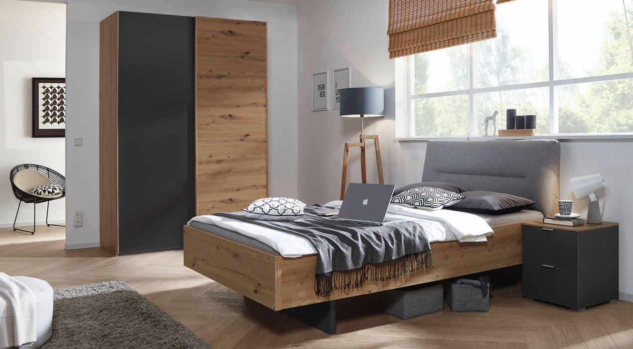 Modernes Jugendzimmer mit Möbeln aus Holz und grauen Akzenten, darunter ein Bett, ein Kleiderschrank und ein funktionaler Schreibtisch. Der Raum ist hell und gemütlich gestaltet