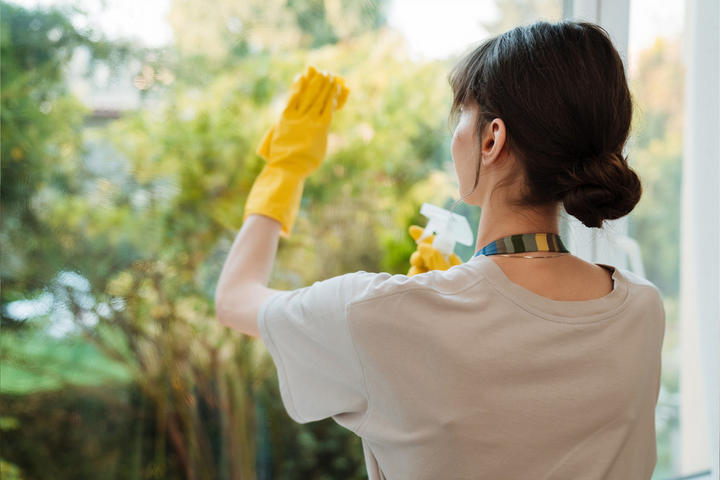 Eine Frau in gelben Handschuhen und weißem Shirt reinigt ein Fenster