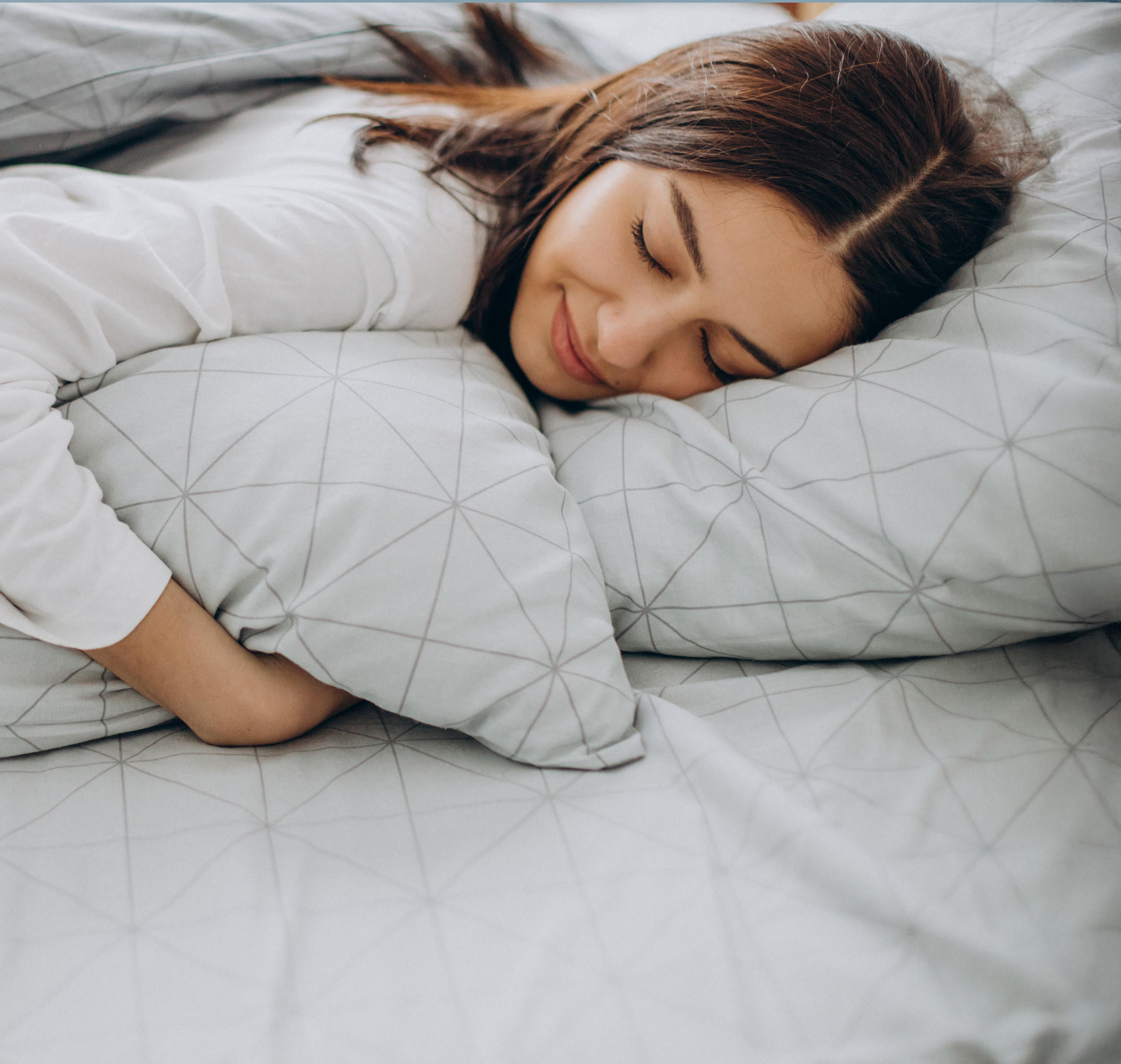 Eine Frau liegt entspannt auf einem Bett mit grauer Decke – Symbol für Abkühlung und Ruhe.