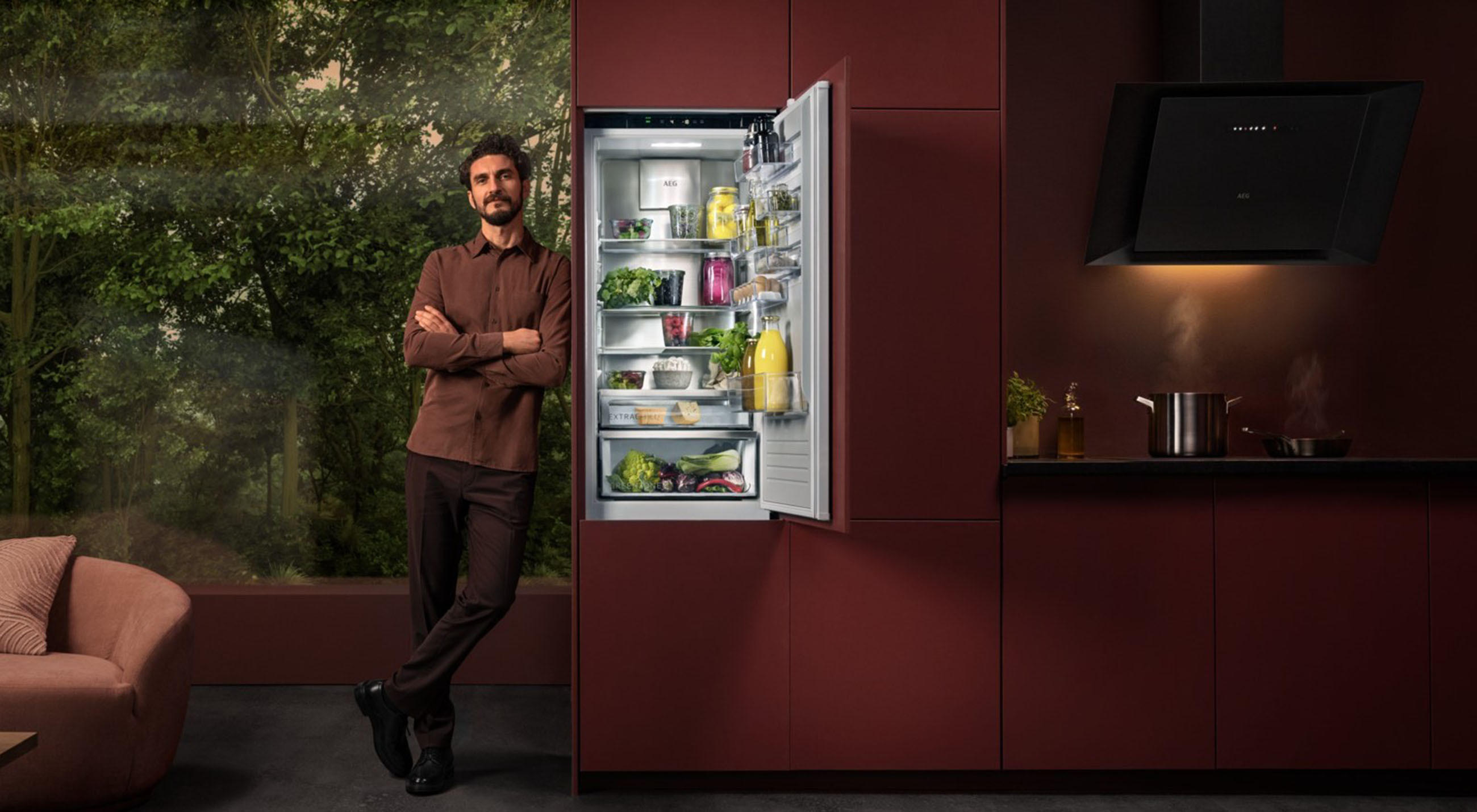 1. Ein Mann steht in einer roten Küche vor einem AEG-Kühlschrank, der mit verschiedenen Lebensmitteln gefüllt ist.