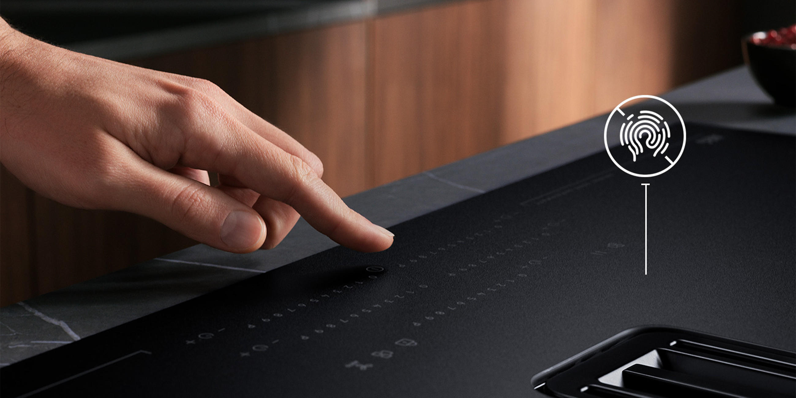 Nahaufnahme: Hand bedient die Touch-Steuerung eines mattschwarzen AEG Induktionskochfelds mit integriertem Dunstabzug; eingeblendetes Fingerabdruck-Icon weist auf die Bedienoberfläche hin.