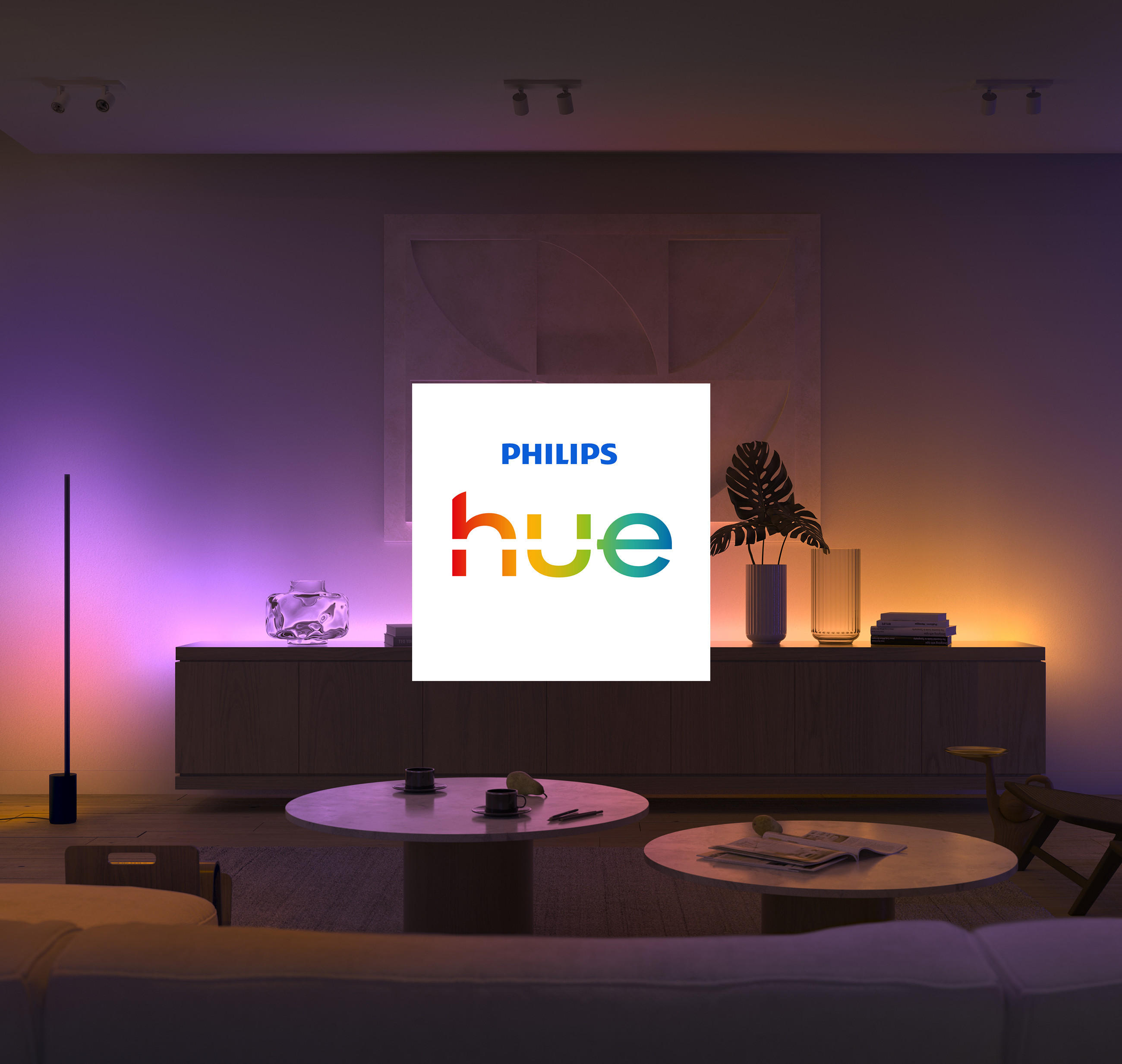Modernes Wohnzimmer mit stimmungsvoller Beleuchtung in Lila- und Orangetönen; in der Mitte steht ein weißes Quadrat mit dem Schriftzug „hue“ - Mit PHILIPS Hue eine völlig neue Lichterfahrung erleben