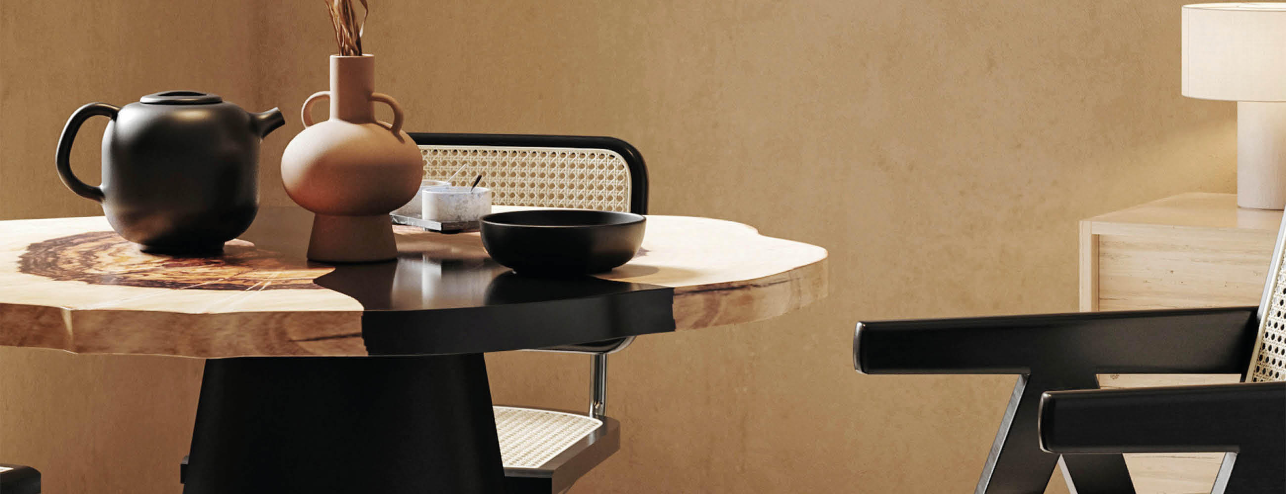 Runder Esstisch mit schwarzer Vase, brauner Vase und schwarzer Schale vor beiger Wand neben Stuhl mit schwarzem Rahmen und Geflechtlehne