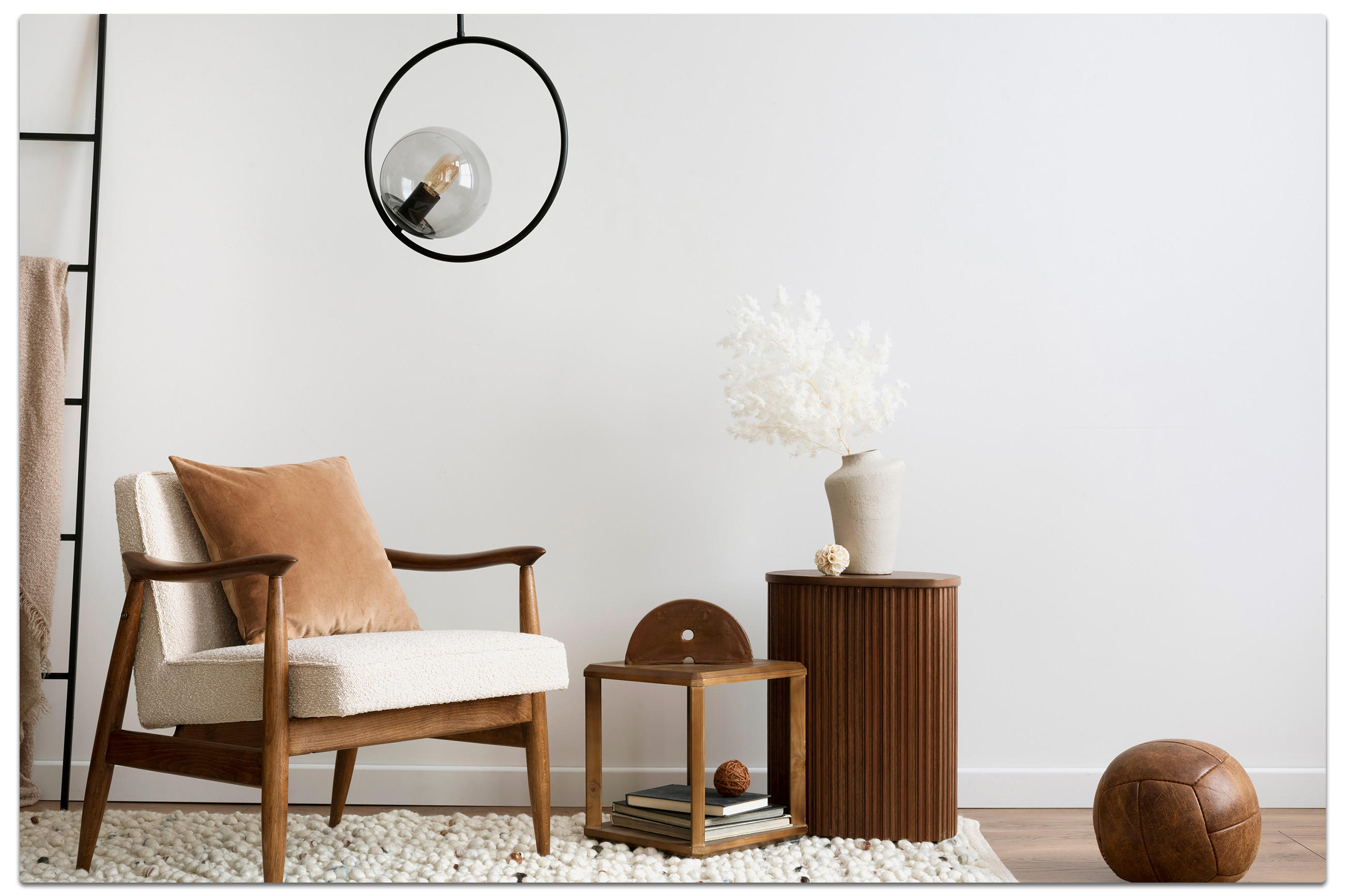 Gemütliche Wohnszene im Cocooning-Stil mit Holzsessel, hellen Polstern, braunem Kissen, Beistelltisch mit Büchern und Deko, geriffeltem Holzschrank mit Vase und Lederhocker – minimalistisches Design mit warmen Materialien.