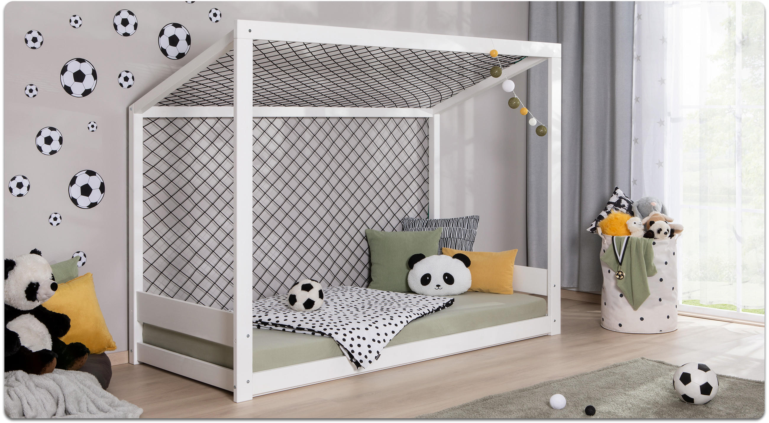 Kinderzimmer mit weißem Hausbett, schwarz-weiß gepunkteter Bettdecke, Panda-Kissen, Fußball-Wandstickern und Spielzeugkorb mit Kuscheltieren.