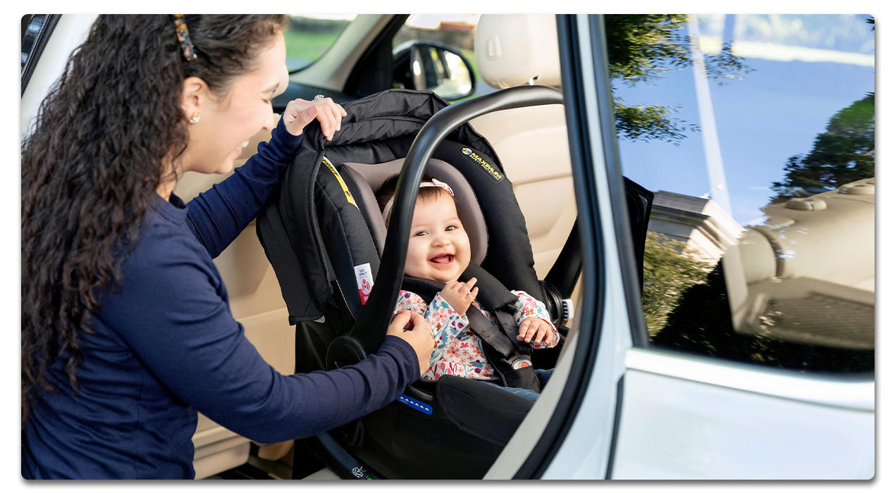 Frau mit baby in der babyschale am auto mit offener autotür