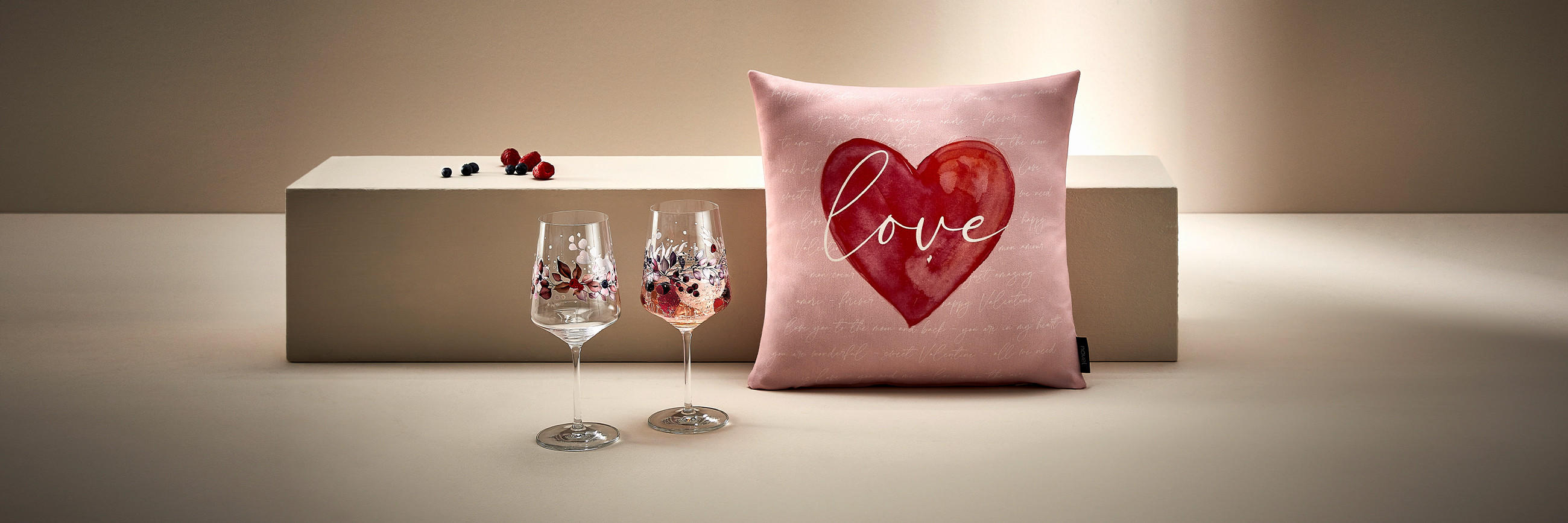  Valentinstagsgeschenke für Frauen: Stilvolle Weingläser mit floralen Mustern und dekoratives rosa Kissen mit rotem Herz und ‚love‘-Schriftzug – romantische Geschenkideen für den Valentinstag.