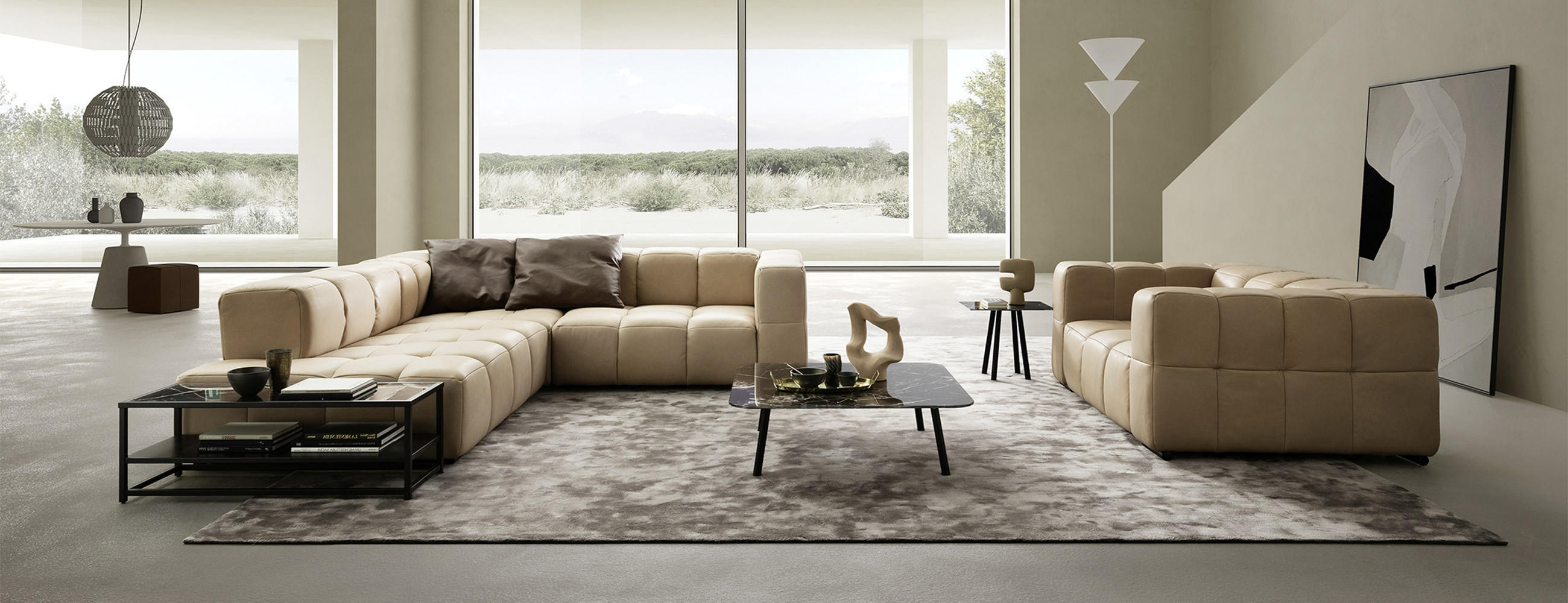Großzügiges, helles Wohnzimmer mit modularer BELLUTI Ecksofa und Bigsofa in Beige auf weichem Teppich; dazu Couchtische mit Deko, Stehleuchte und bodentiefe Fensterfront mit Blick ins Grüne.