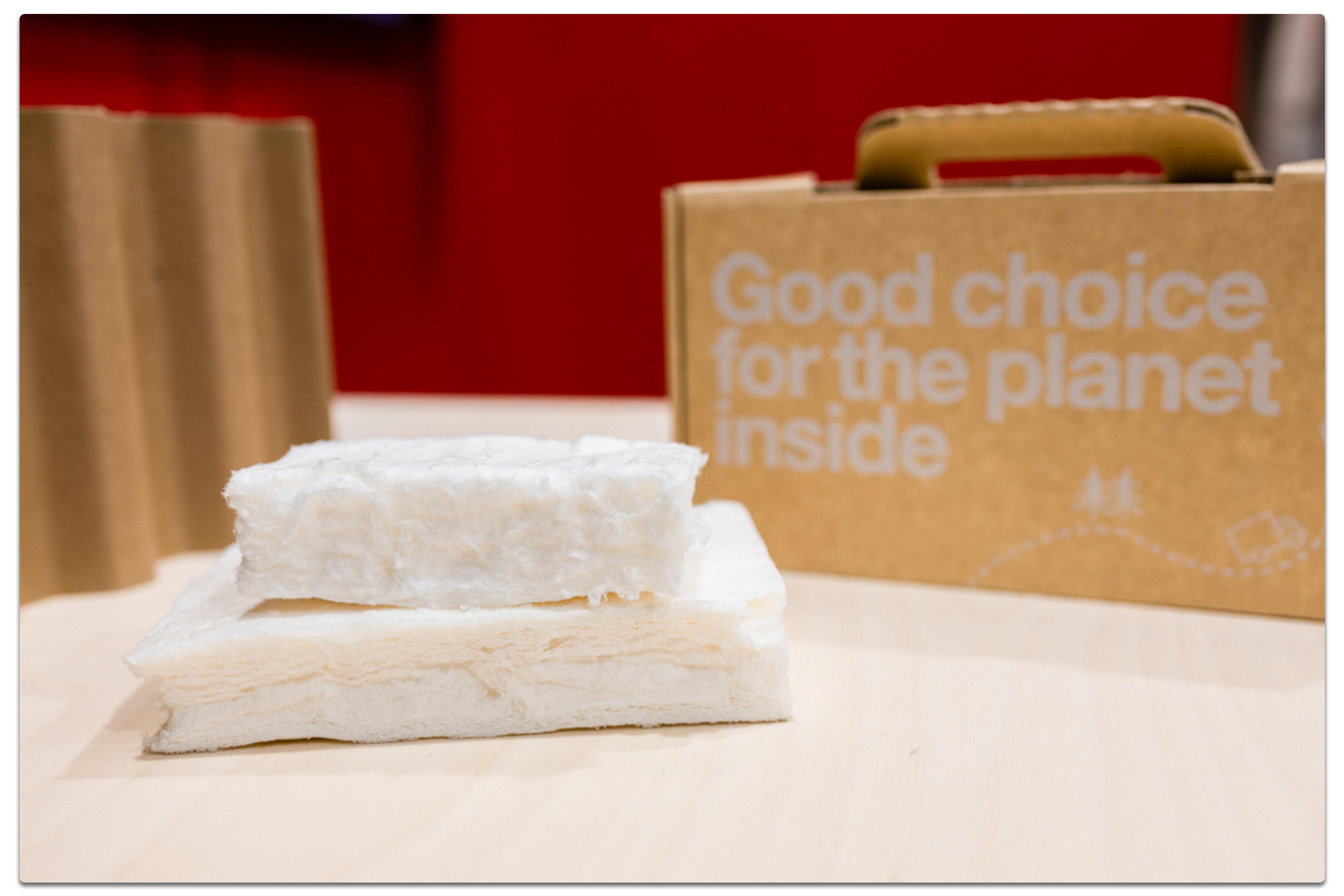 Zwei Stücke weißes, faseriges Material auf einer hellen Oberfläche. Rechts davon ist ein brauner Karton mit dem Text "Good choice for the planet inside