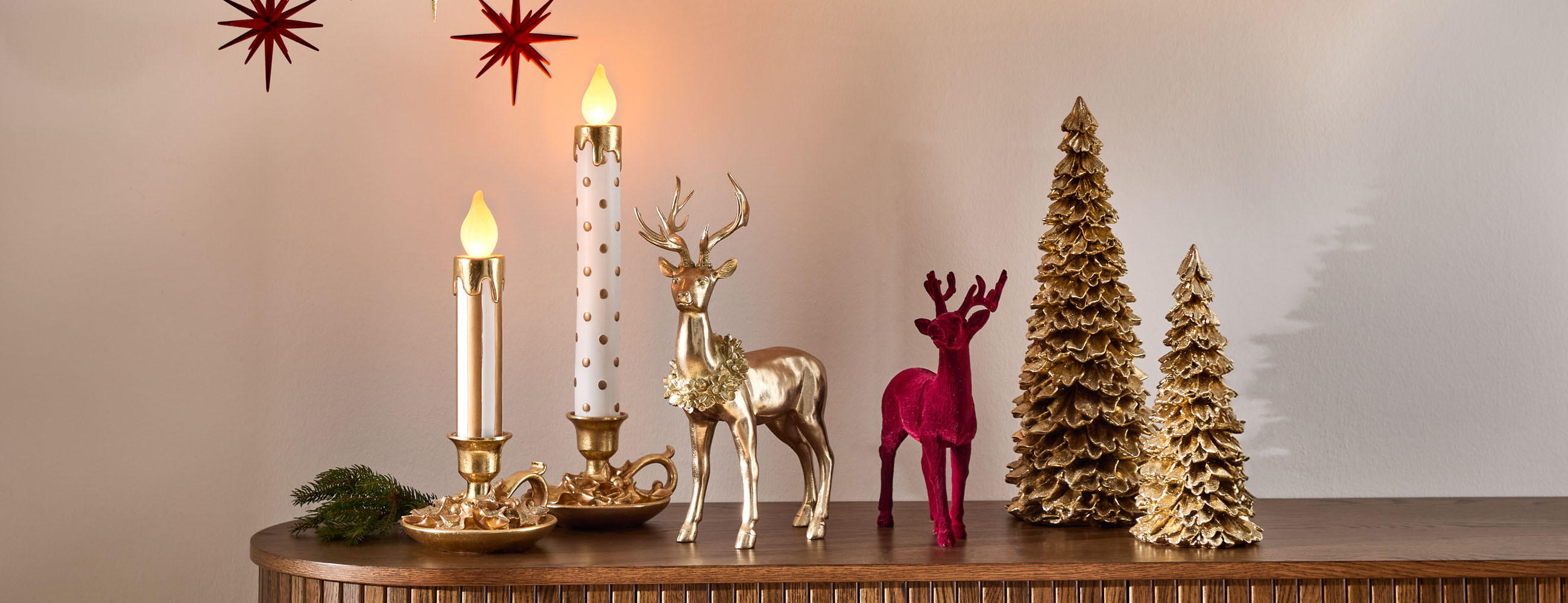 Festliche Szene mit zwei goldenen Kerzenhaltern, roten und goldenen Rentierfiguren sowie goldenen Weihnachtsbaum-Dekorationen auf Holzfläche.