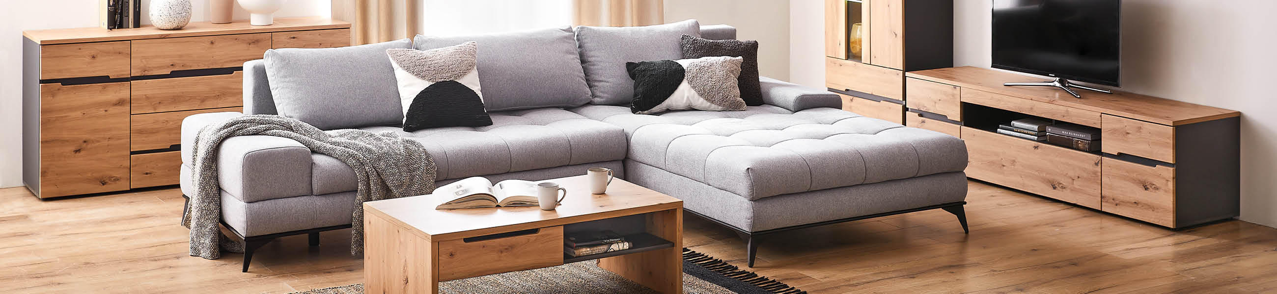 Modernes Wohnzimmer mit grauem Sofa, Holzmöbeln und TV-Schrank.