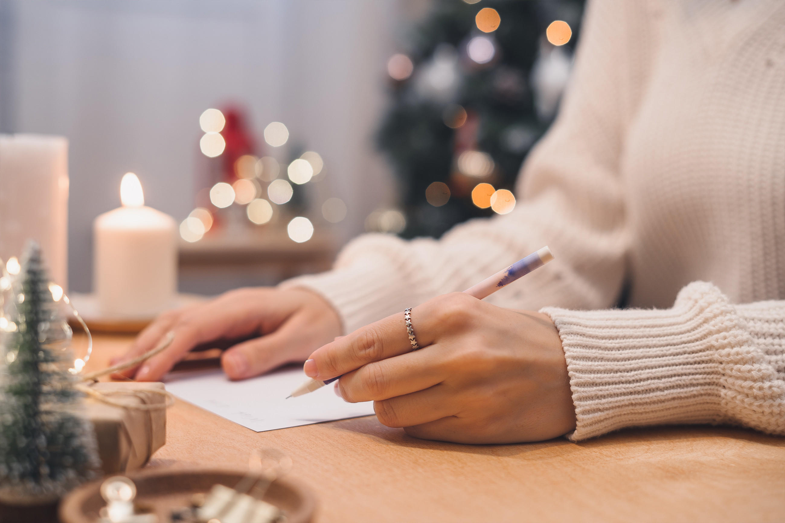 Eine Frau verfasst eine Weihnachtskarte an einem liebevoll gedeckten Tisch