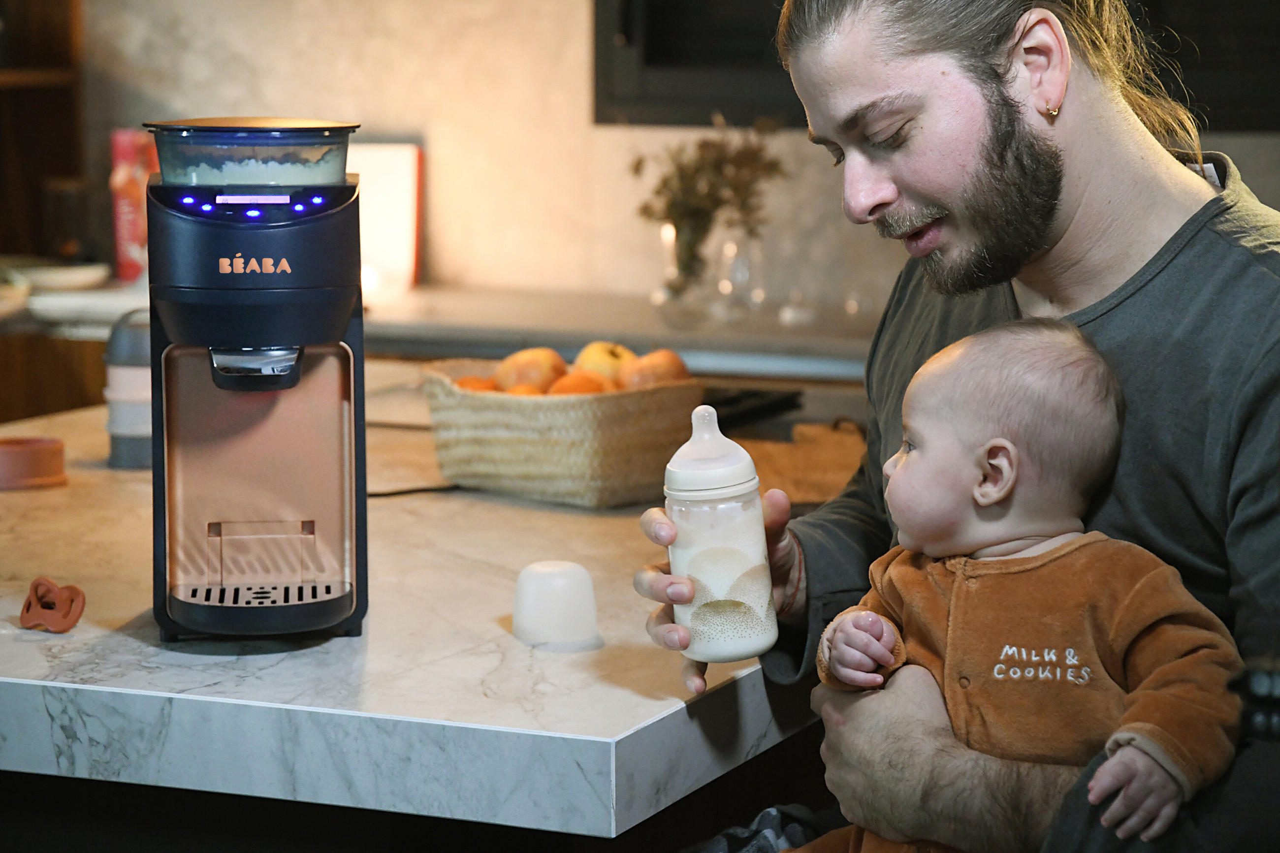 Junge Vater mit Baby auf dem Schoß nutzt den Babykostwärmer von Béaba.