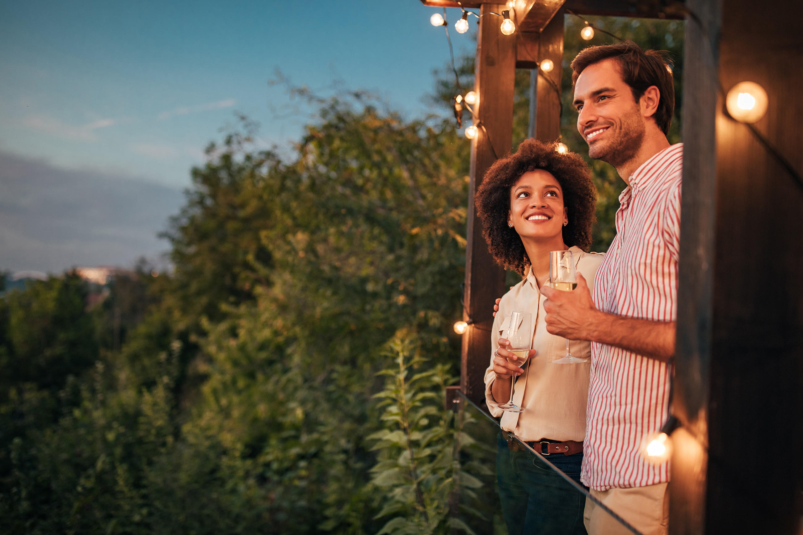 Ein Mann und eine Frau stehen auf einer Terrasse, umgeben von Lichtern, und genießen einen Sommerabend im Garten.