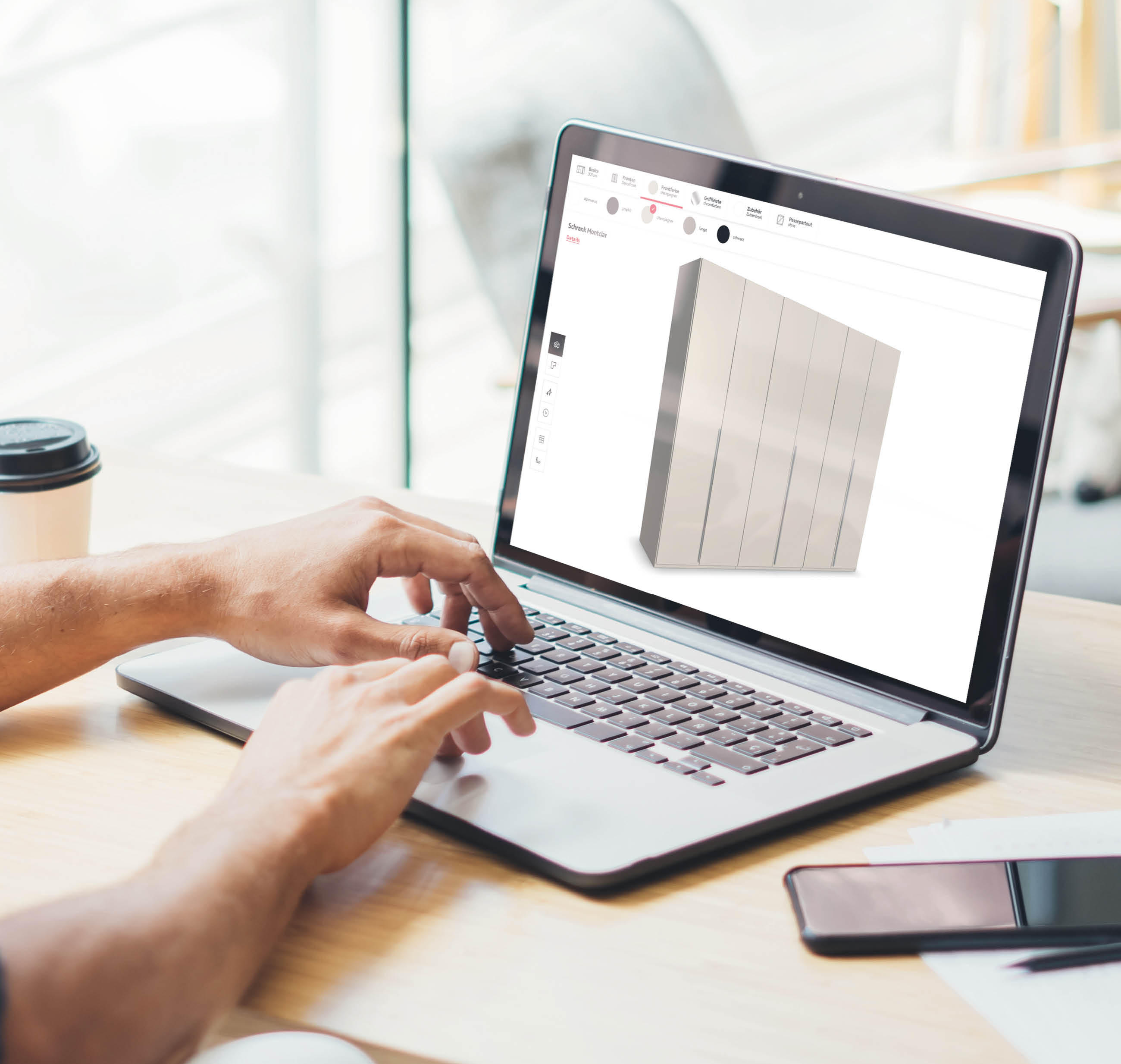 Person tippt auf Laptop mit 3D-Modell eines Schrankes auf dem Bildschirm, daneben Smartphone und Kaffeebecher auf Holztisch.