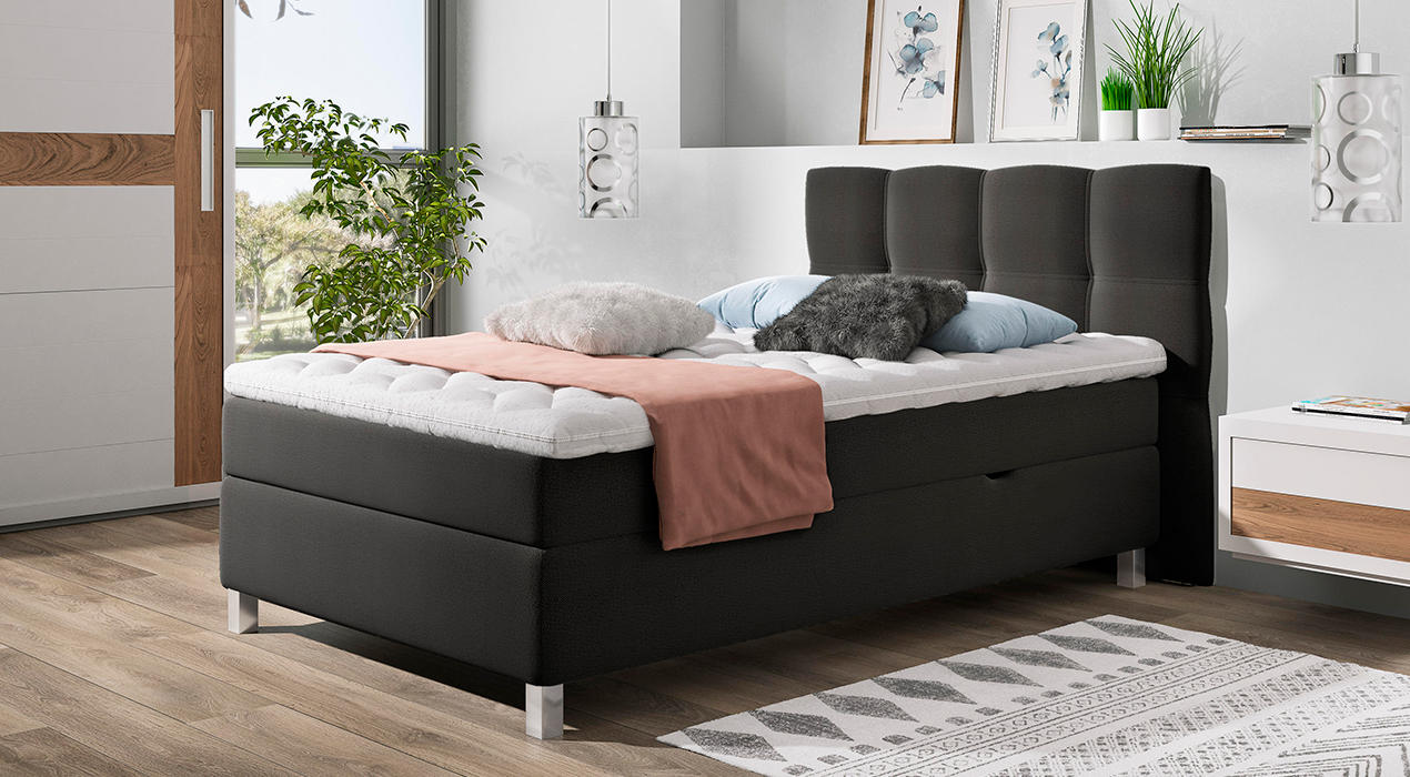 Schwarzes Boxspringbett mit Steppung im Kopfteil und weißem Topper.
