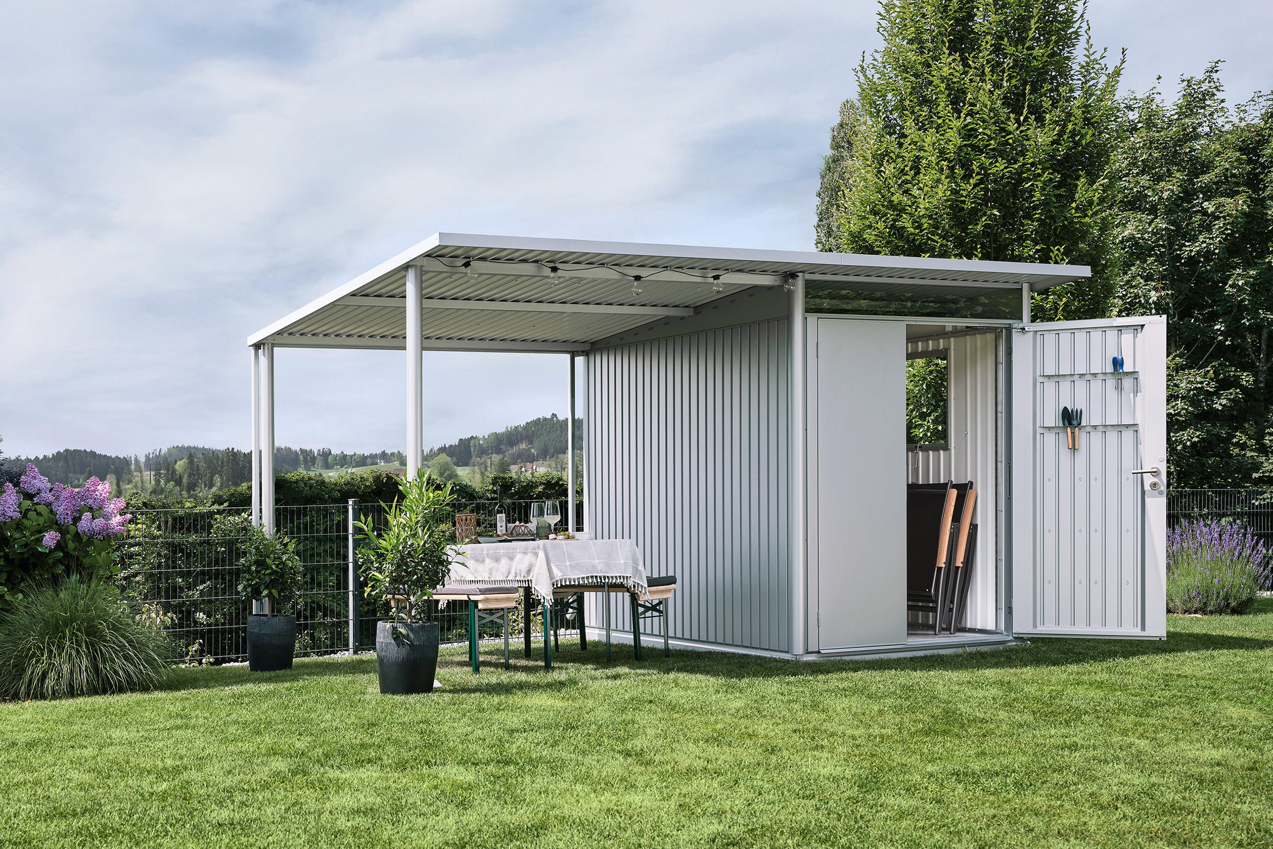 LIEBHERR Metallgerätehaus auf grüner Wiese mit Bank unter dem Vordach.