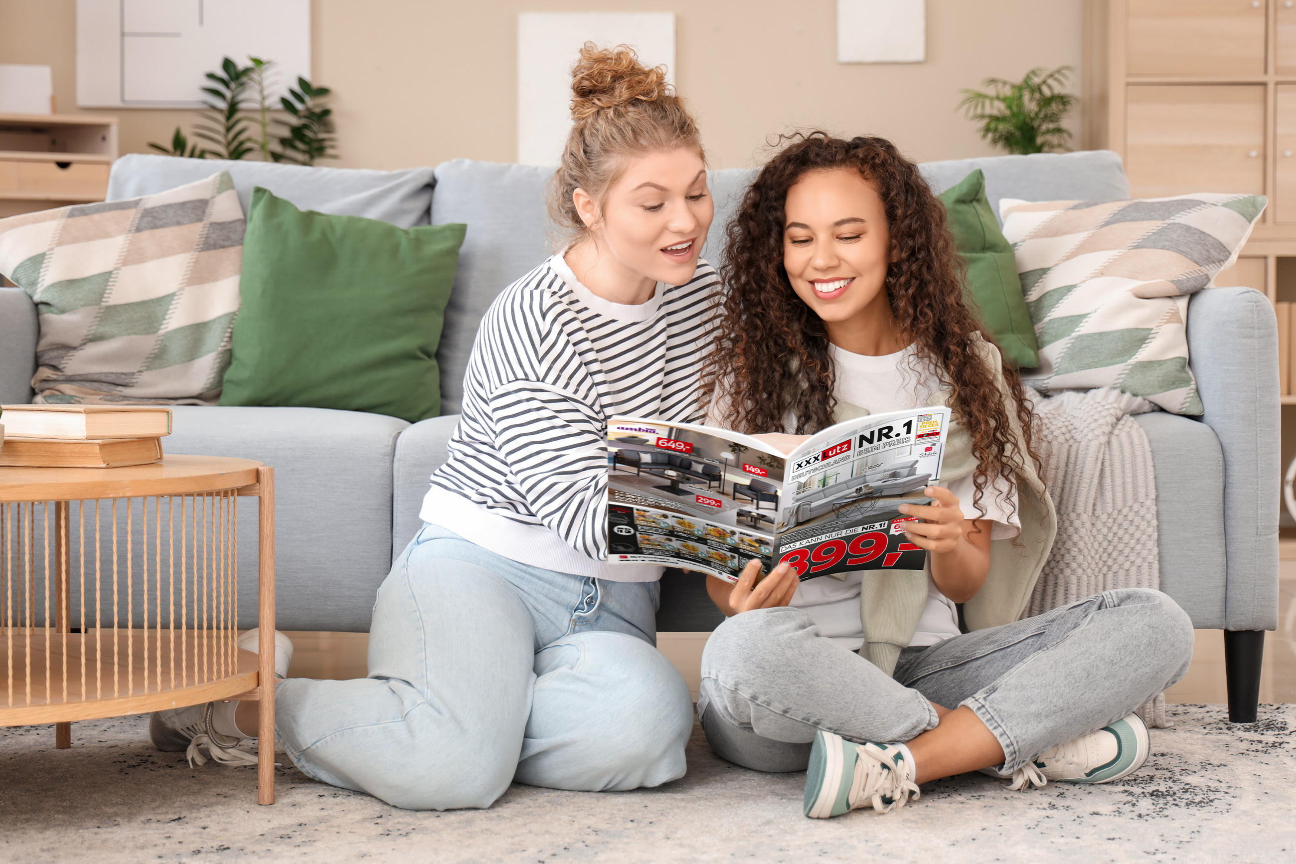 Zwei Personen entdecken Angebote im XXXLutz Freundschaftskartenjournal, gemütlich im Wohnzimmer mit Sofa und Beistelltisch.