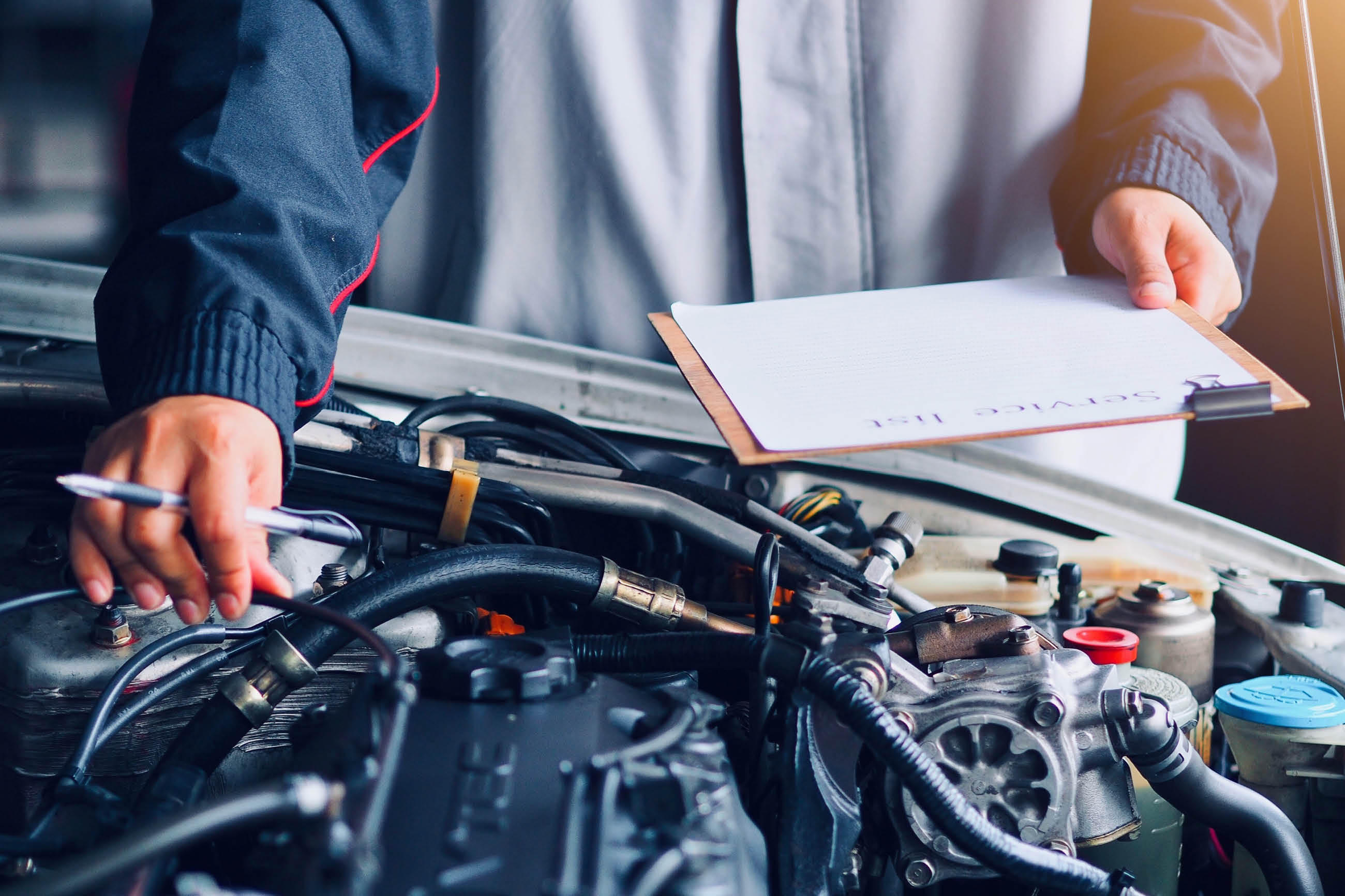 Person überprüft den Motorraum eines Autos und hält eine Checkliste in der Hand.