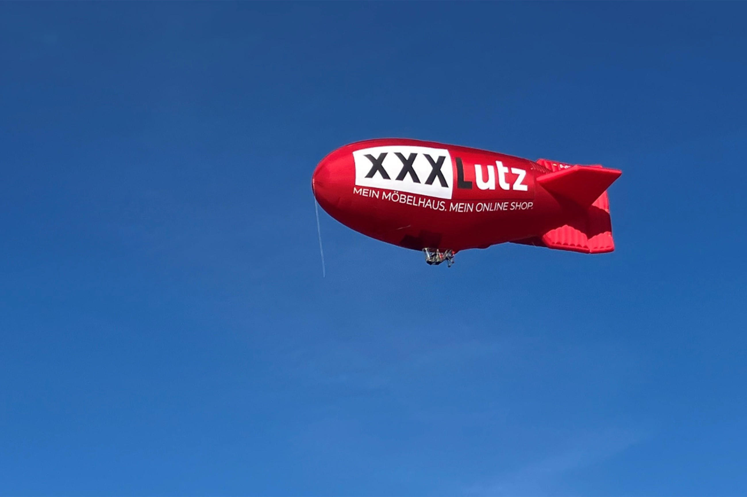 Roter Zeppelin mit XXXLutz-Logo am Himmel.