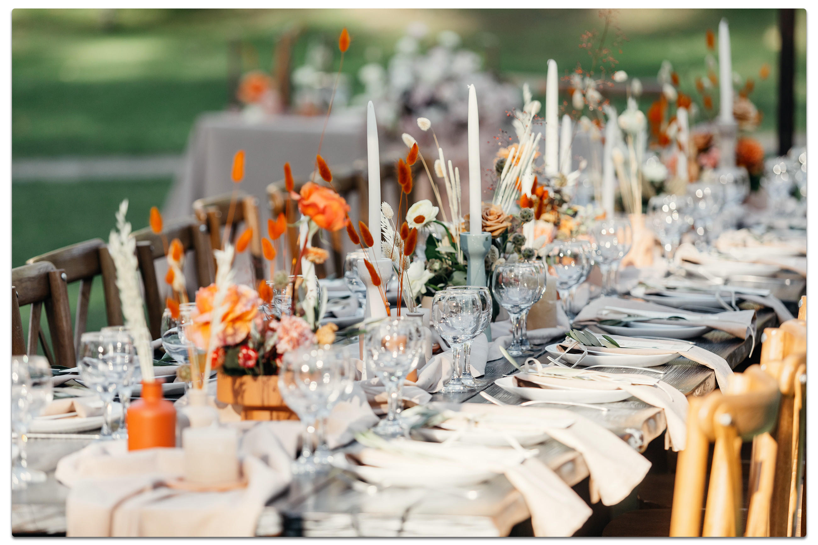 Ein langer Tisch mit weißen und orangen Blumen, dekoriert für eine Gartenhochzeit im Freien.
