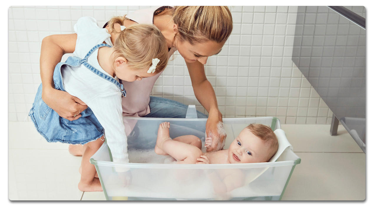 Frau und Kind schauen auf baby in der Badewanne mit wasser und viel schaum