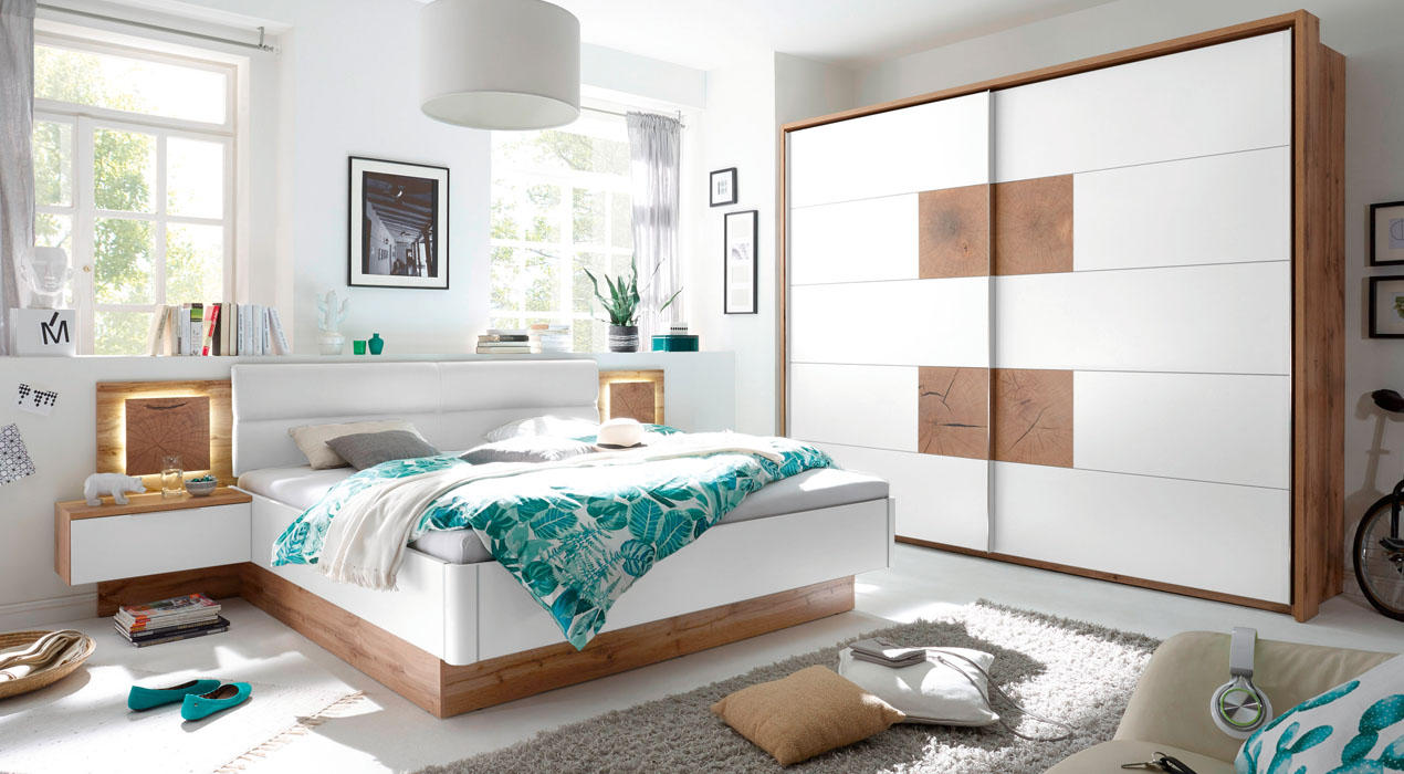 Modernes Schlafzimmer mit weiß-türkiser Bettwäsche im Blumenmuster, Nachttischen mit Lampen, Regal hinter dem Bett und Schiebetürenschrank