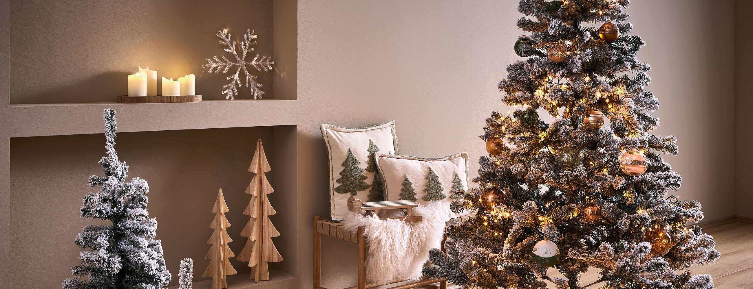 Weihnachtlich dekoriertes Wohnzimmer mit großem beleuchtetem Tannenbaum, Kerzen, Holzdeko und gemütlichem Sessel mit Kissen.