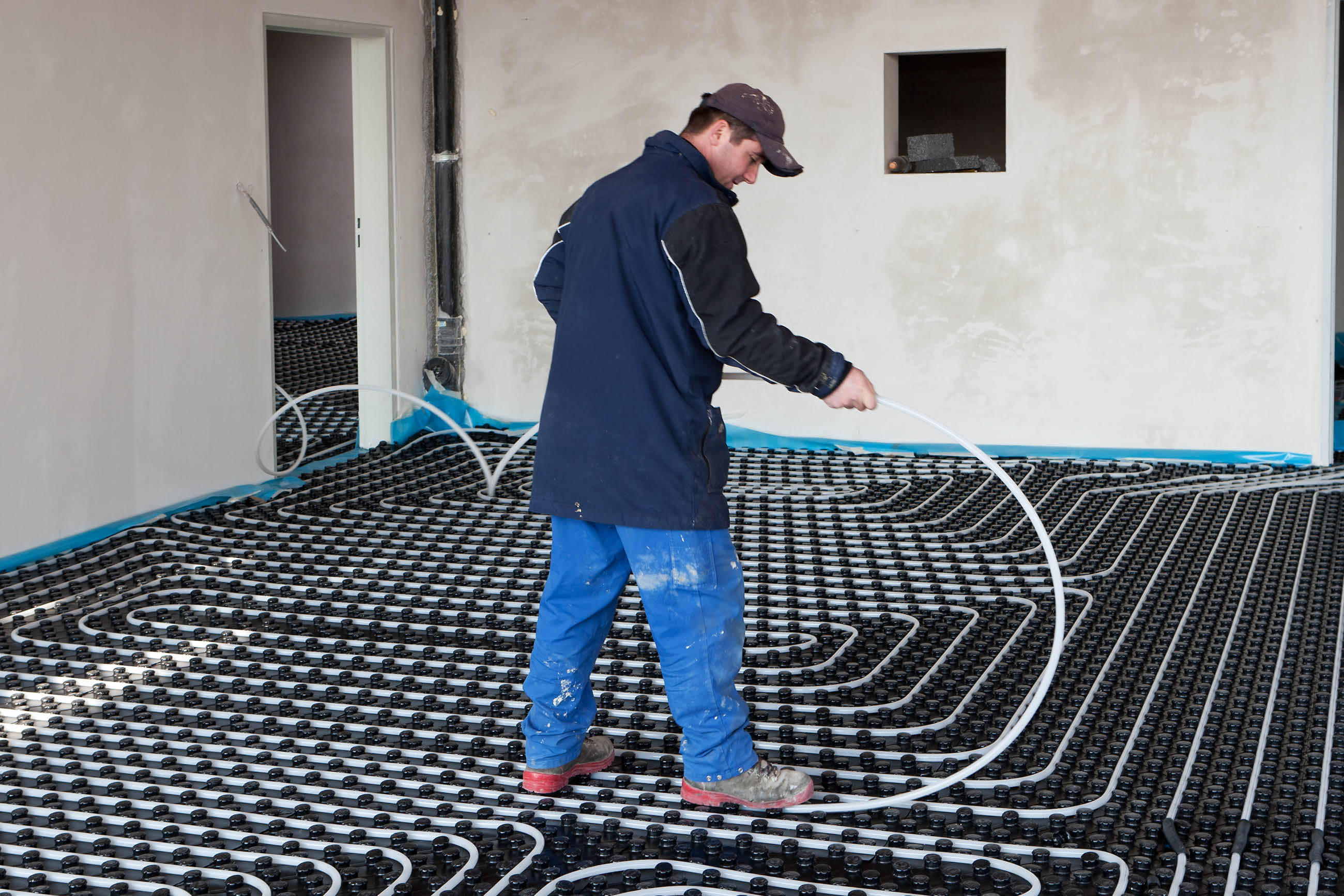 Handwerker verlegt Rohre für eine Fußbodenheizung in einem Raum mit unvollendeten Wänden.