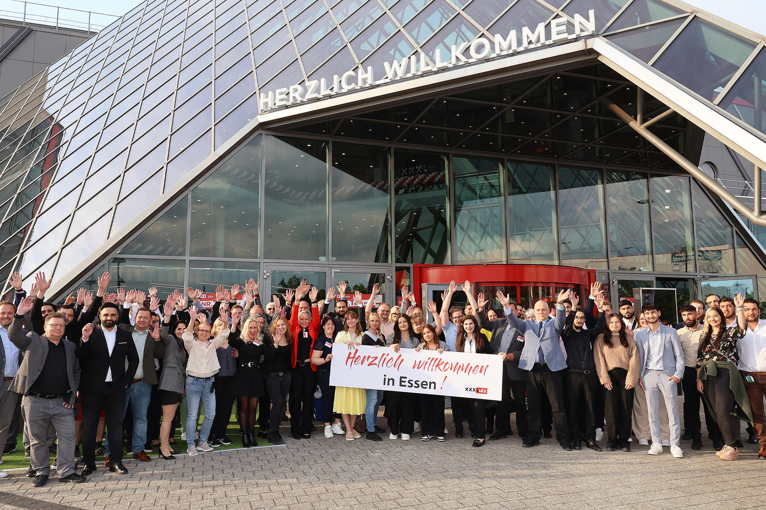 Eine Gruppe von Menschen steht vor dem XXXLutz-Gebäude zur Neueröffnung in Essen.