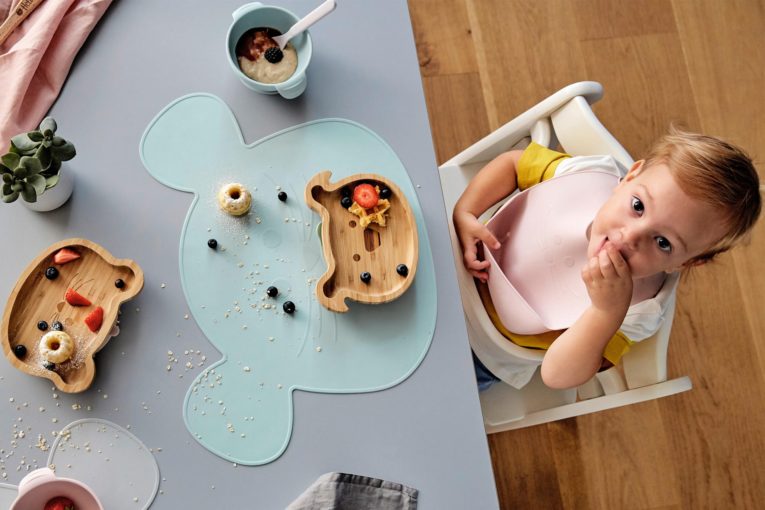 Baby sitzt am Tisch und ist Früchte aus einem tükisenem Teller