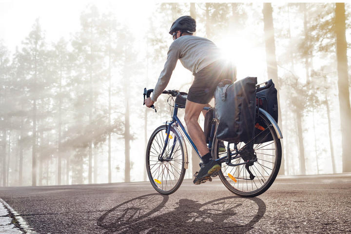 Ein Mann fährt morgens mit einer Fahrradtasche auf dem Rad einen Weg entlang.