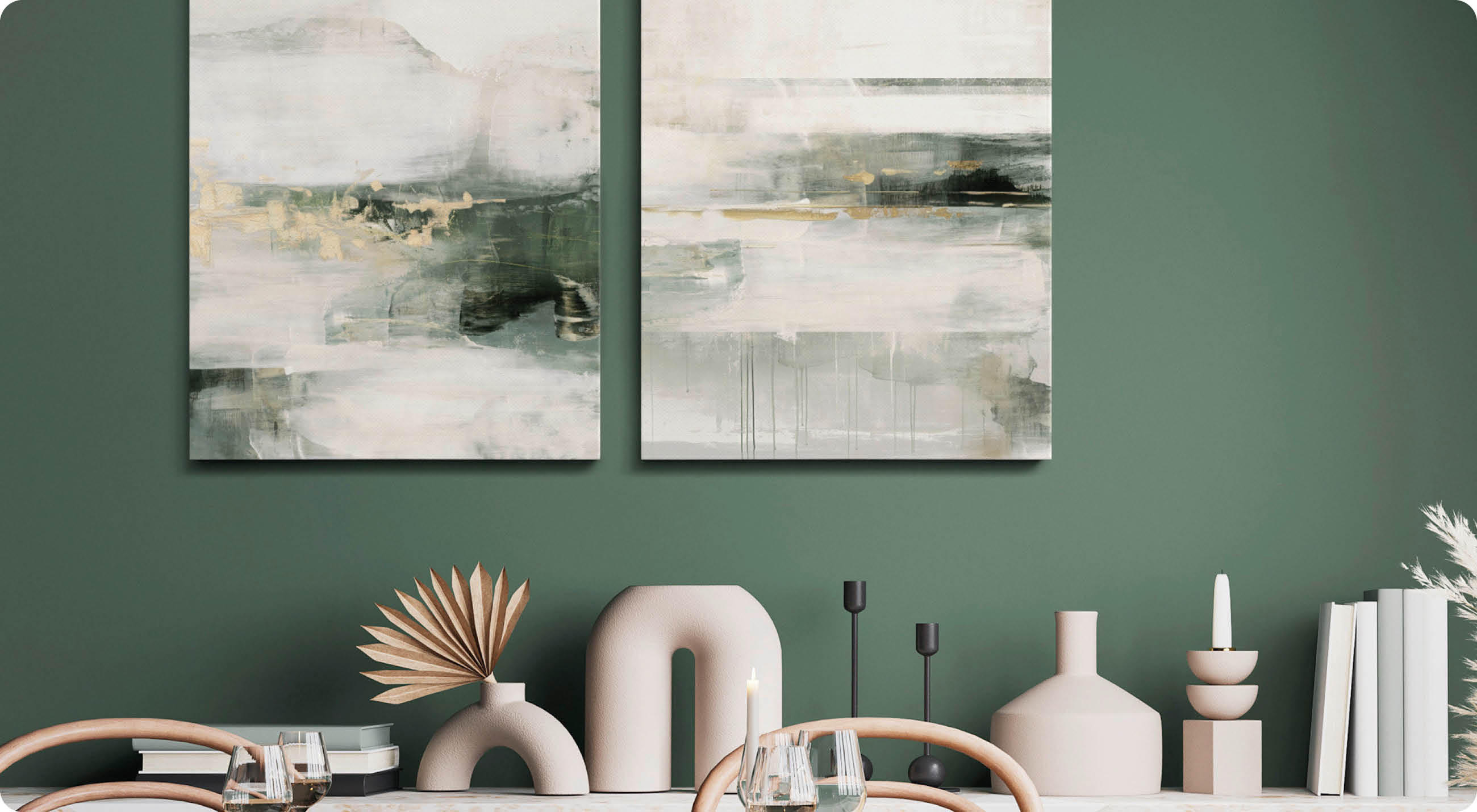 Zwei abstrakte, quadratische Gemälde mit hellen und dunklen Farbschichten hängen an einer dunkelgrünen Wand über einem Tisch mit dekorativen Vasen und Kerzenhaltern.