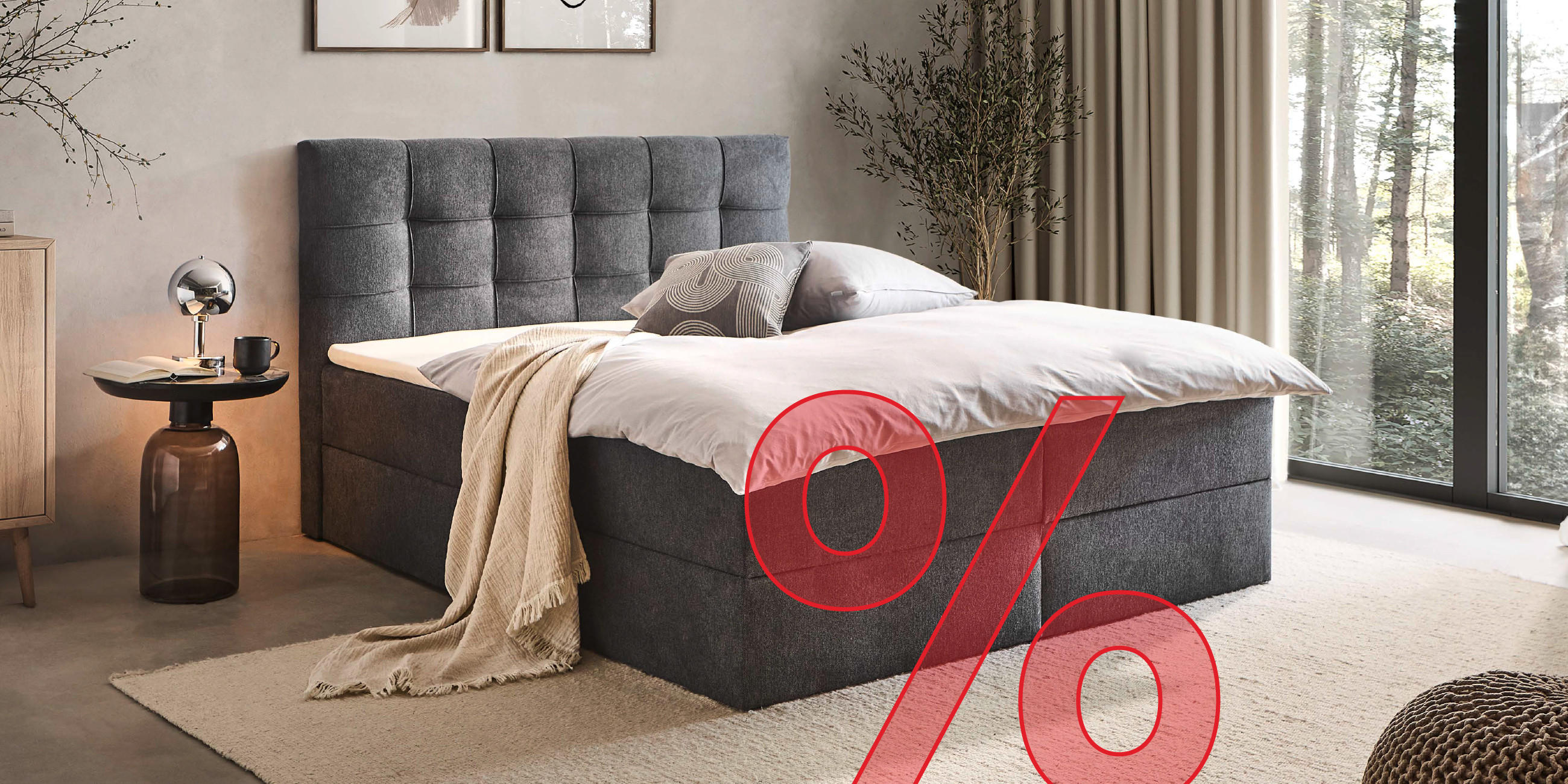 Dunkelgraues Boxspringbett mit Schlaftextilien, Nachttisch und Lampe gemütlich eingerichtet