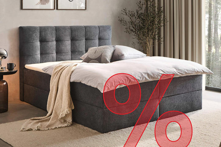 Dunkelgraues Boxspringbett mit Schlaftextilien, Nachttisch und Lampe gemütlich eingerichtet