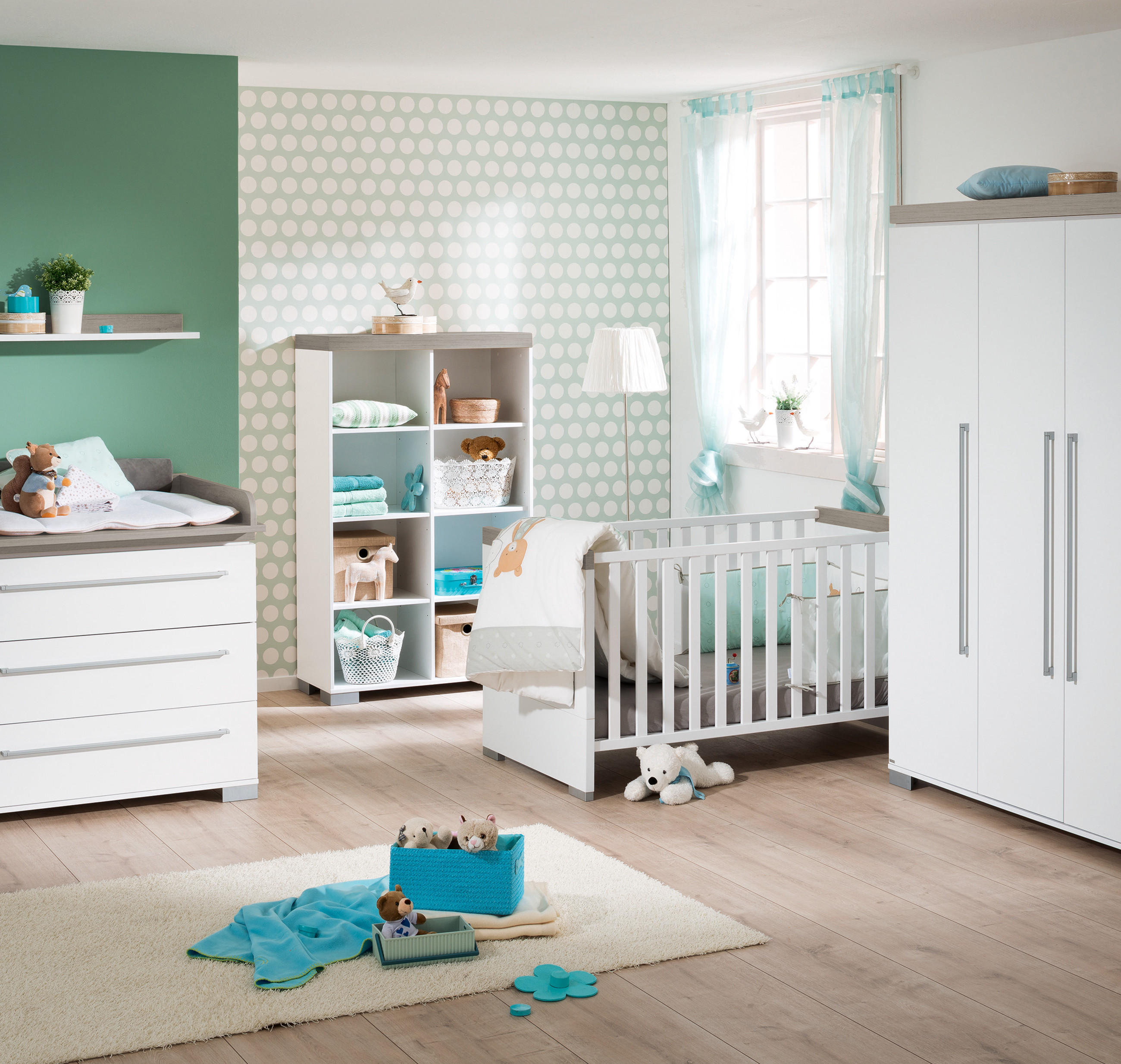 Kinderzimmer mit Wickelkommode, Regal, Kinderbett und Kleiderschrank in hellem Holz und Weiß vor grüner Wand.