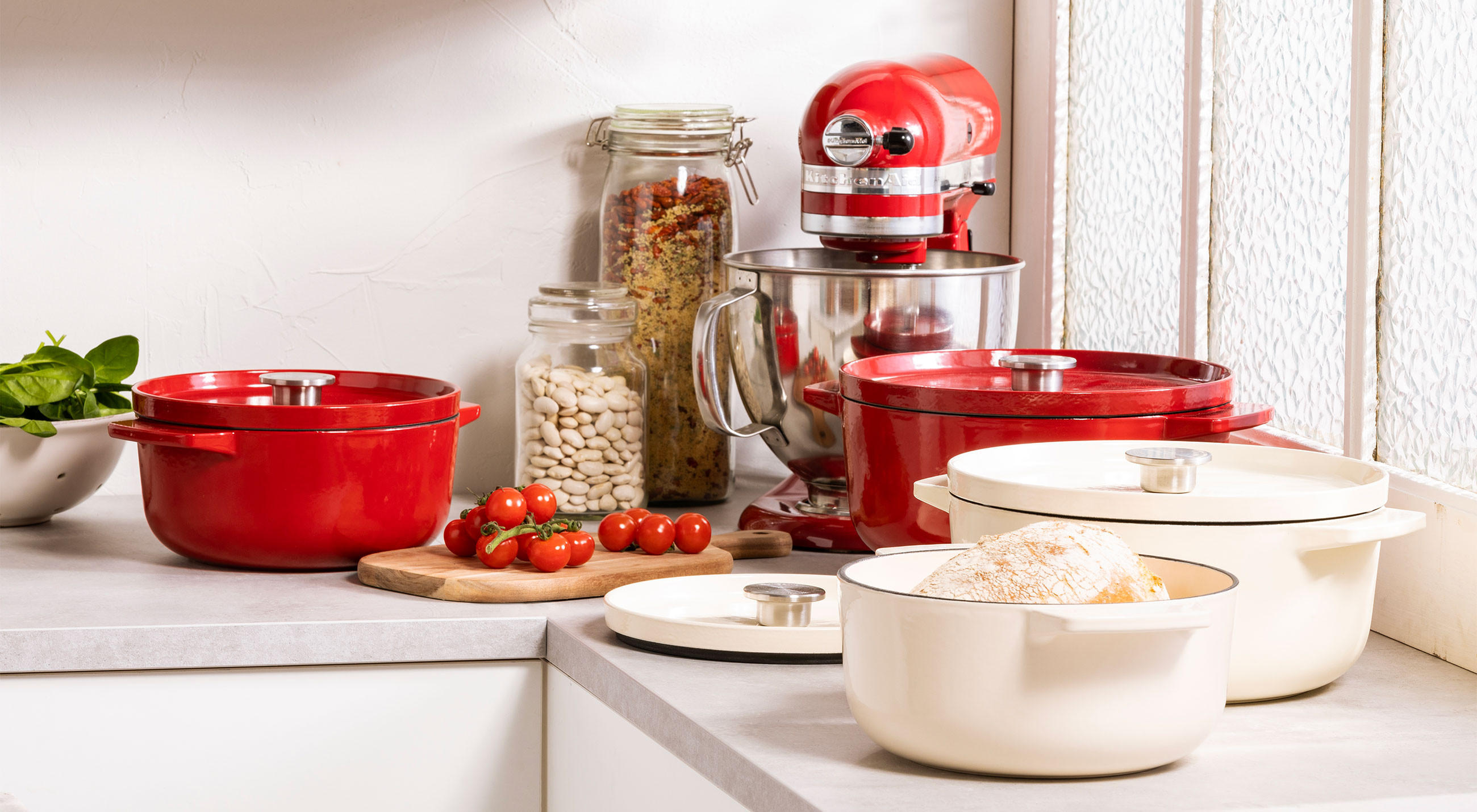 Küchengeräte, Töpfe und Pfannen von KitchenAid auf einer Arbeitsplatte in einer modernen Küche.