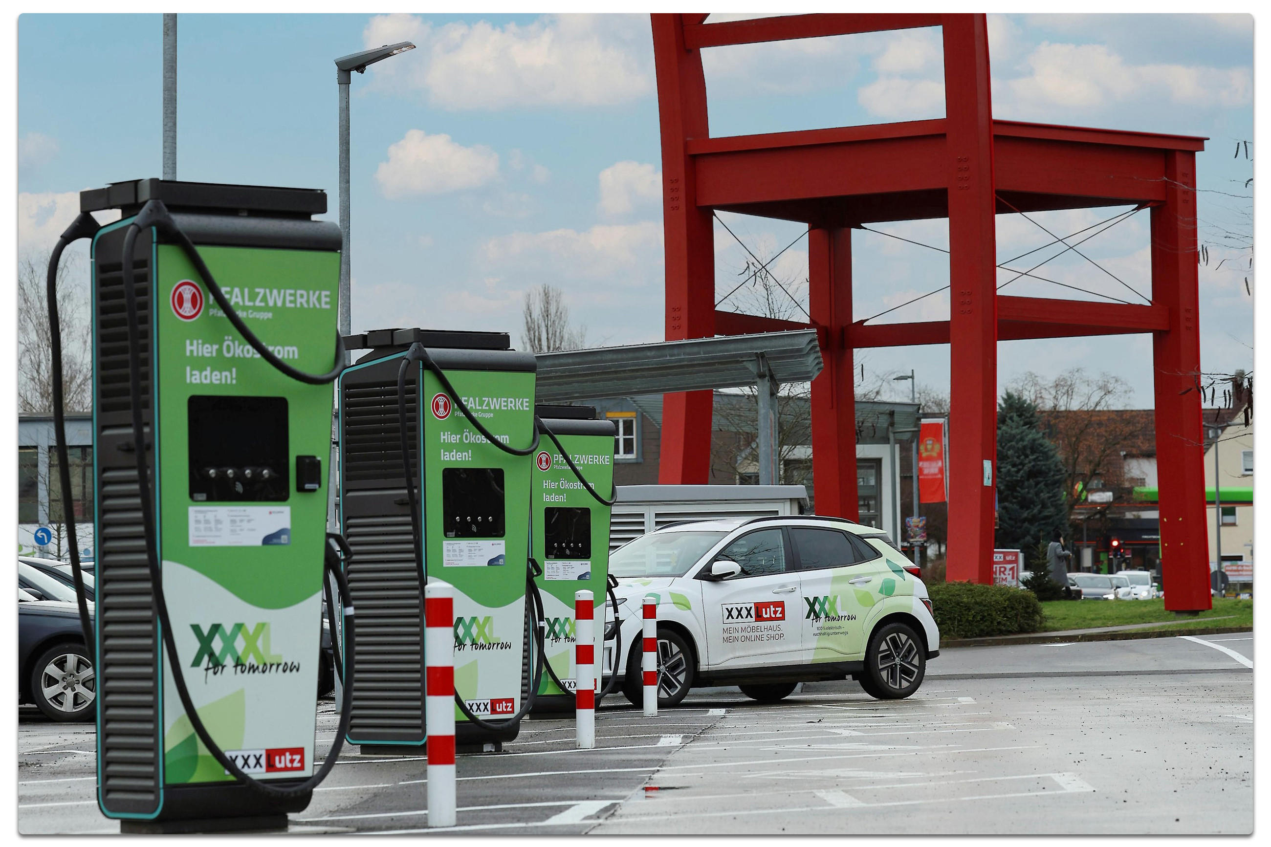 Eine Ladestation für Elektrofahrzeuge mit drei grünen Ladesäulen der Firma "XXXLUTZ" und einem geparkten Elektroauto