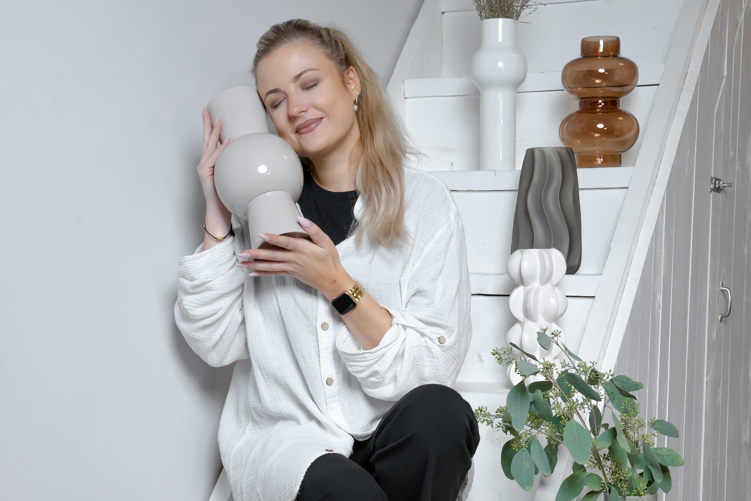 Eine Frau sitzt auf einer Treppe und hält sich eine Vase von Boltze Home and die Wange. 