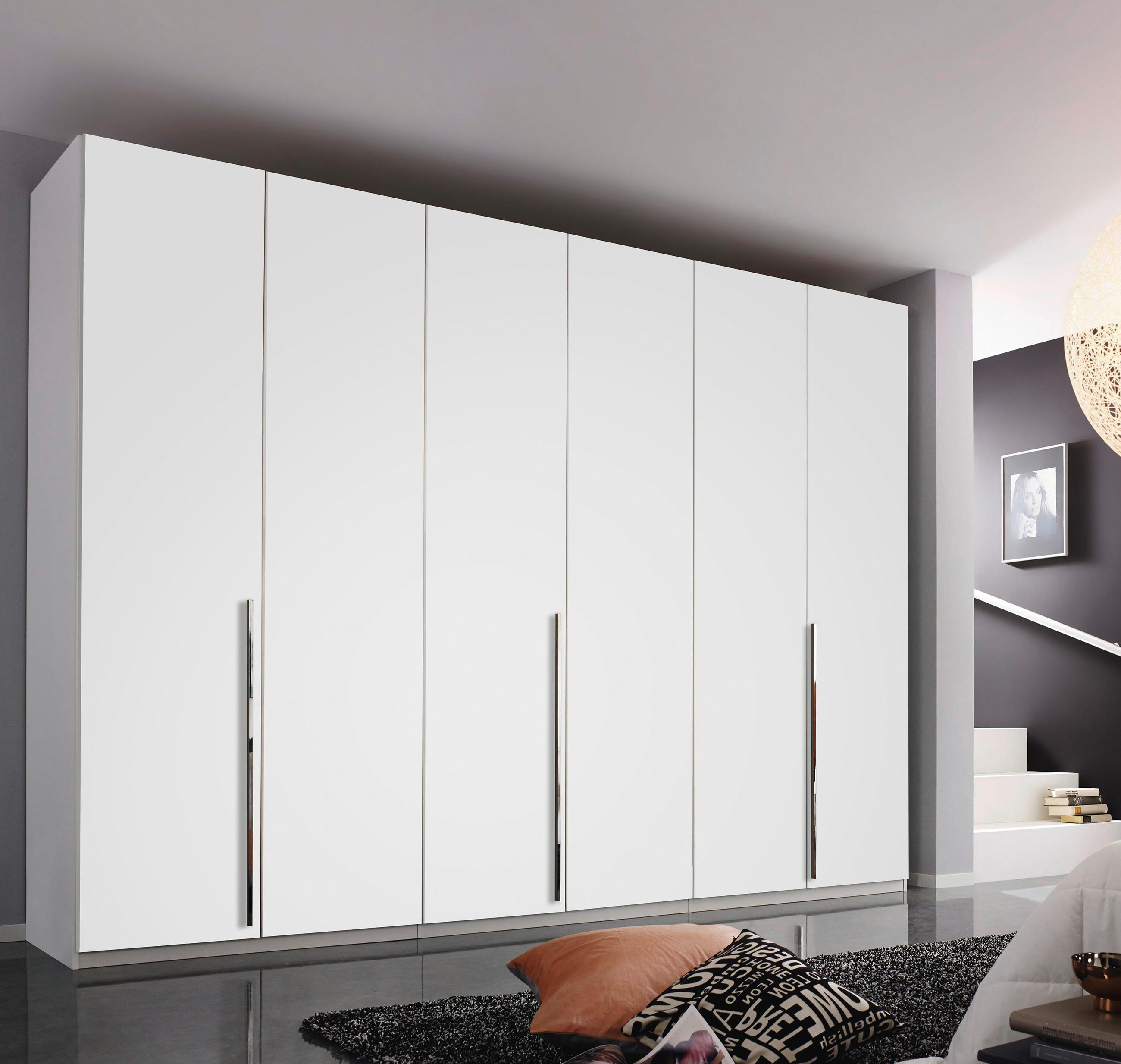 Großer weißer Kleiderschrank mit mehreren Türen und langen Griffen in modernem Schlafzimmer; rechts Bett, Teppich und große Fensterfront mit Lampe.