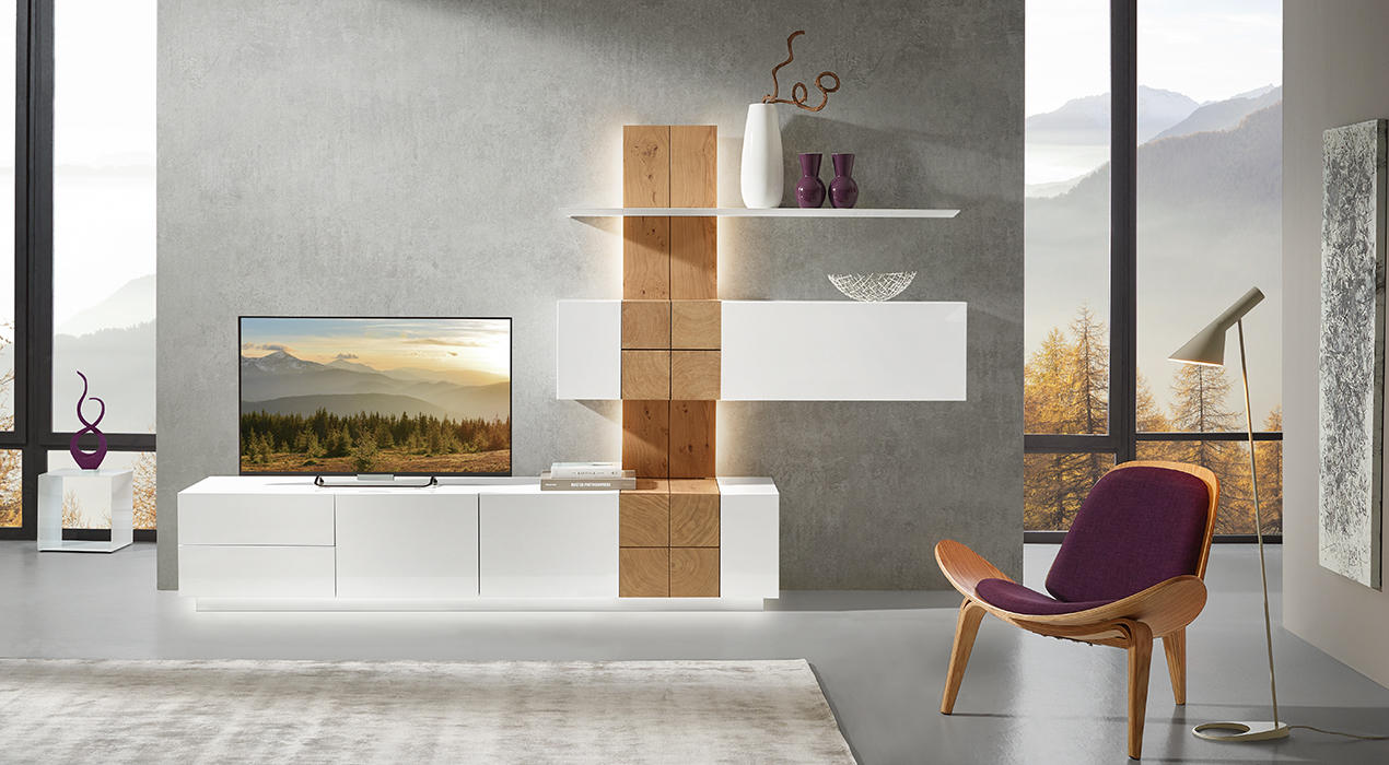 Modernes Wohnzimmer mit weißem TV-Möbel, dekorativen Regalen, lila Sessel, Stehlampe und großem Fenster mit Blick auf Bäume und Berge