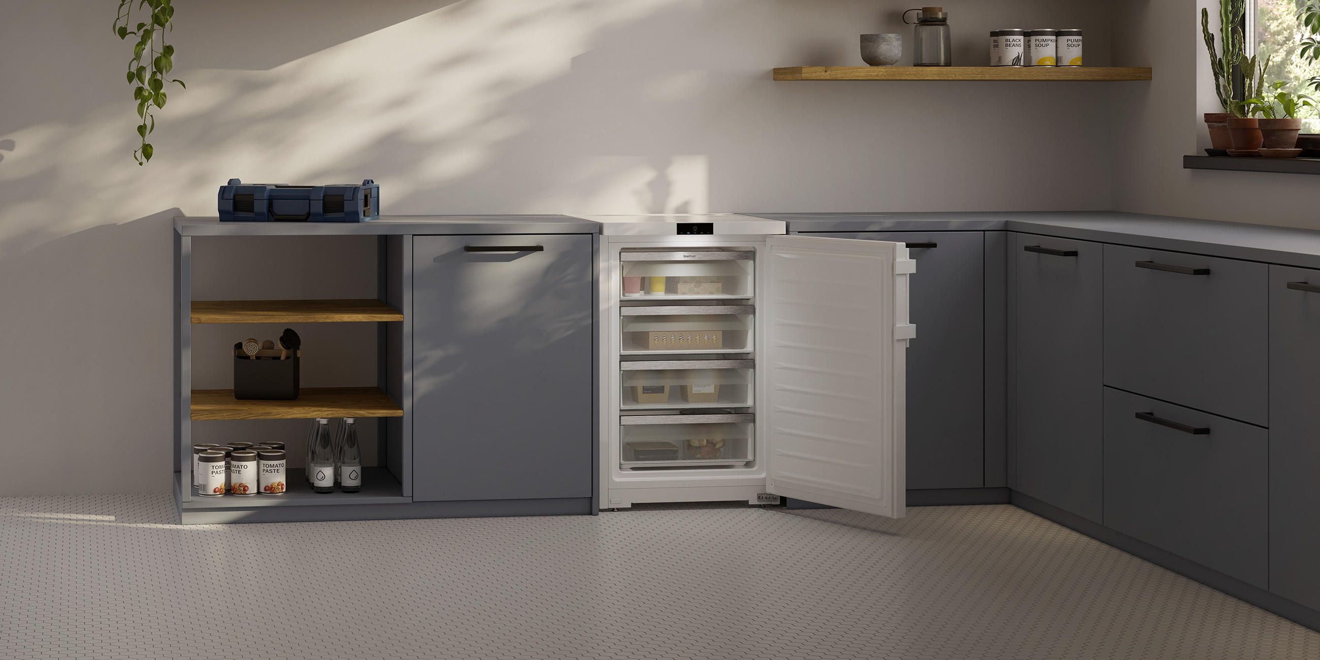 Moderne, platzsparende Küchenzeile in Dunkelgrau mit offenem Unterbau-Kühlschrank und Gefrierschubladen; daneben Regalfach mit Vorräten und Flaschen, darüber schlichtes Wandregal und Fenster mit Pflanzen.