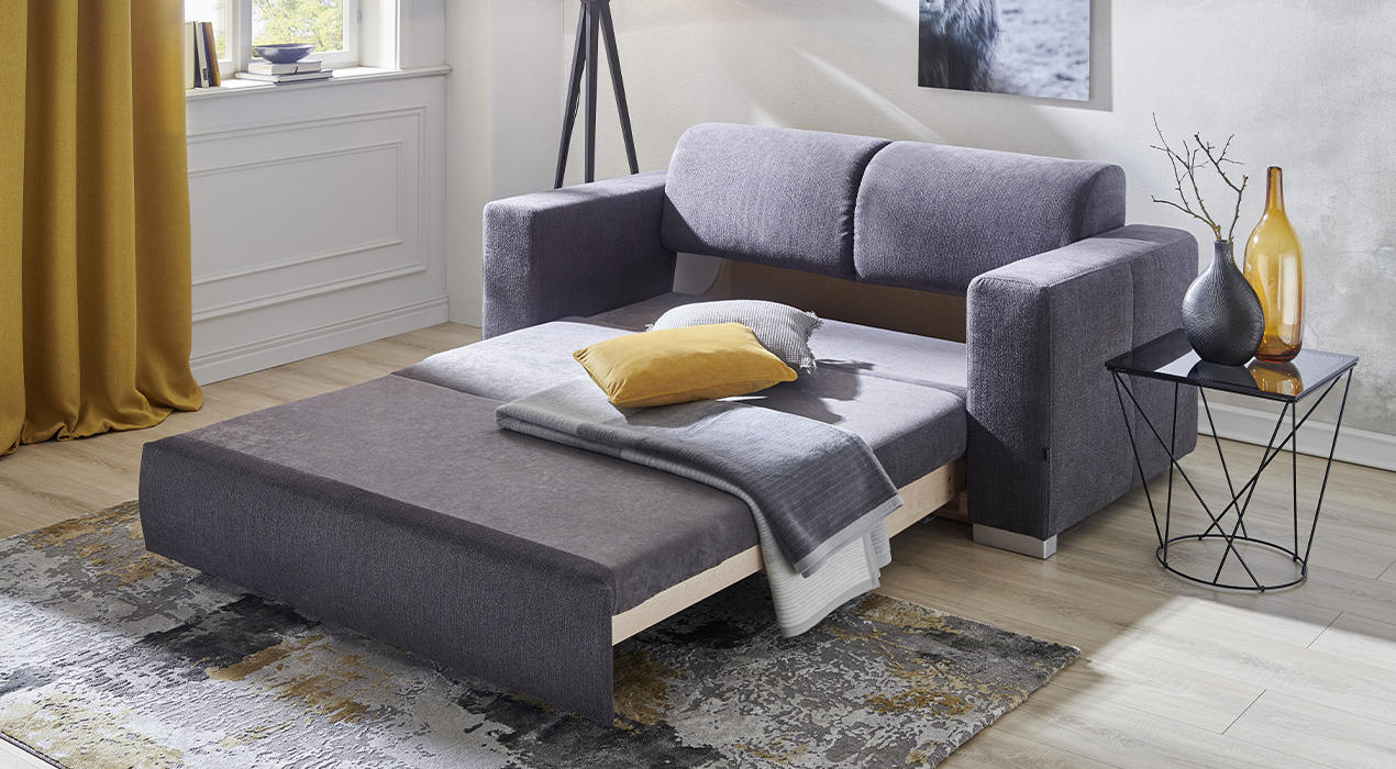 Kleines graues Schlafsofas in ausgezogener Position mit Kissen und Decke.
