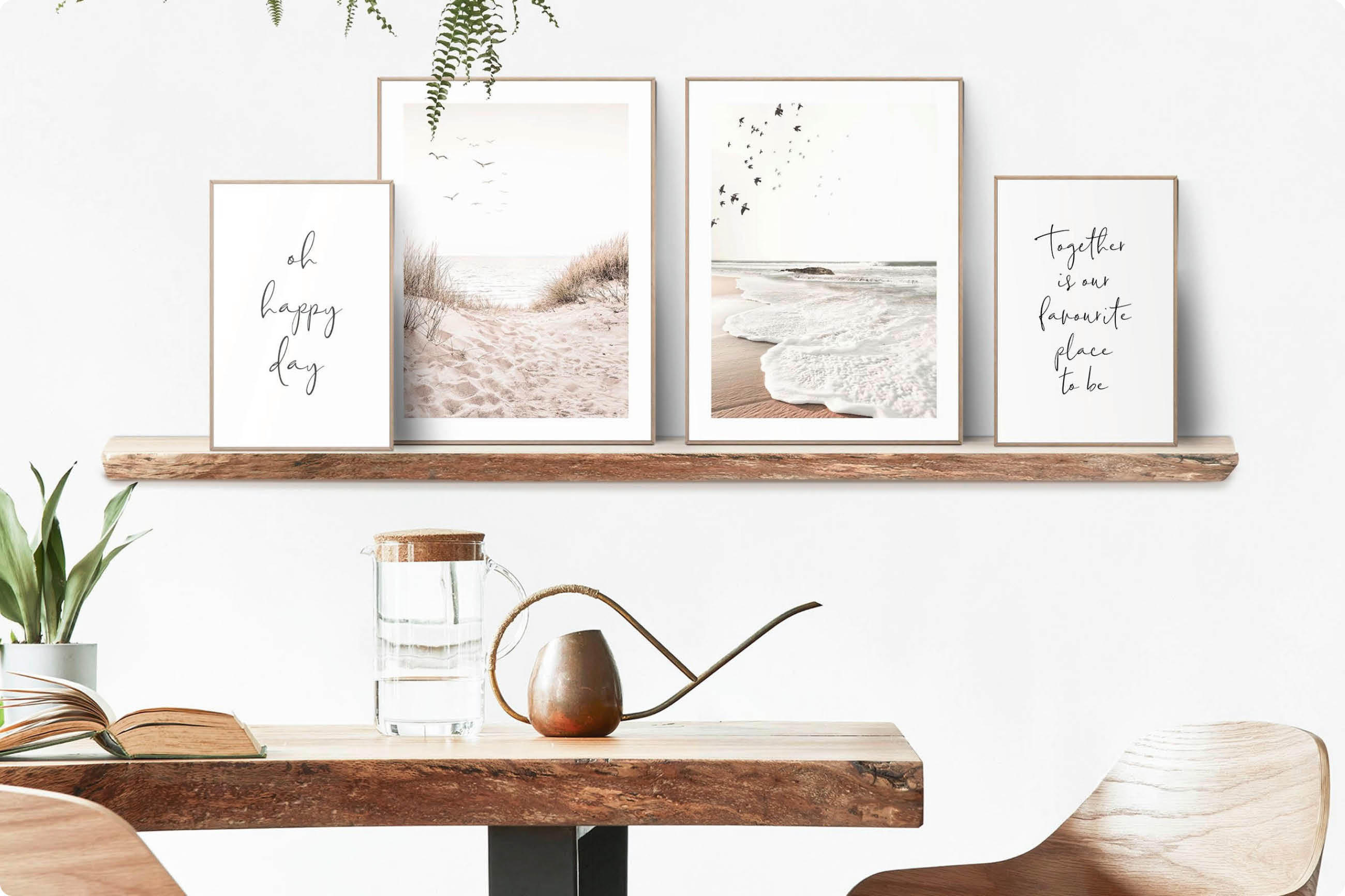 Vier gerahmte Bilder mit Strandmotiven und Schriftzügen auf einem Holzregal über einem Holztisch mit Glas, Gießkanne und Stuhl