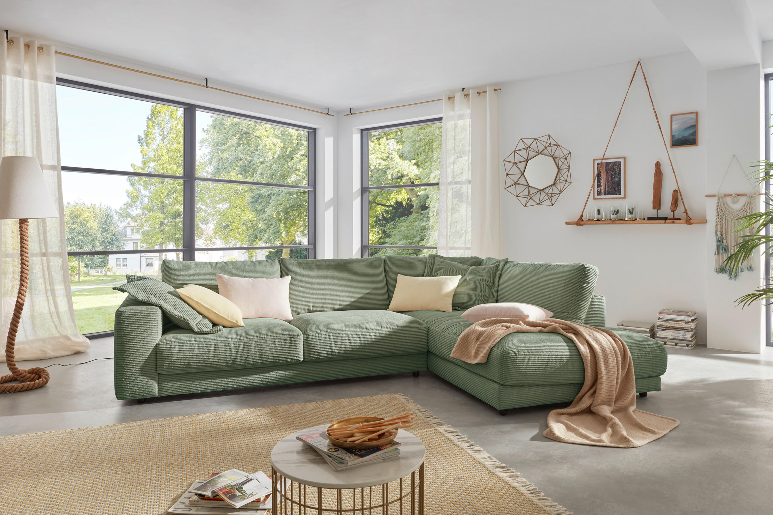 Helles Wohnzimmer mit grünem Ecksofa, großem Fenster, rundem Couchtisch und Wanddekoration.