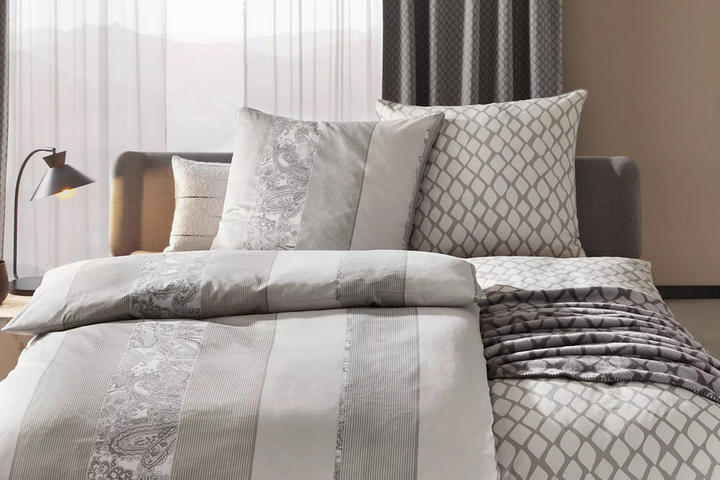 Helle Bettwäsche mit unterschiedlichen Mustern auf Decken und Kissen mit modernem Nachtisch und Nachtischlampe.